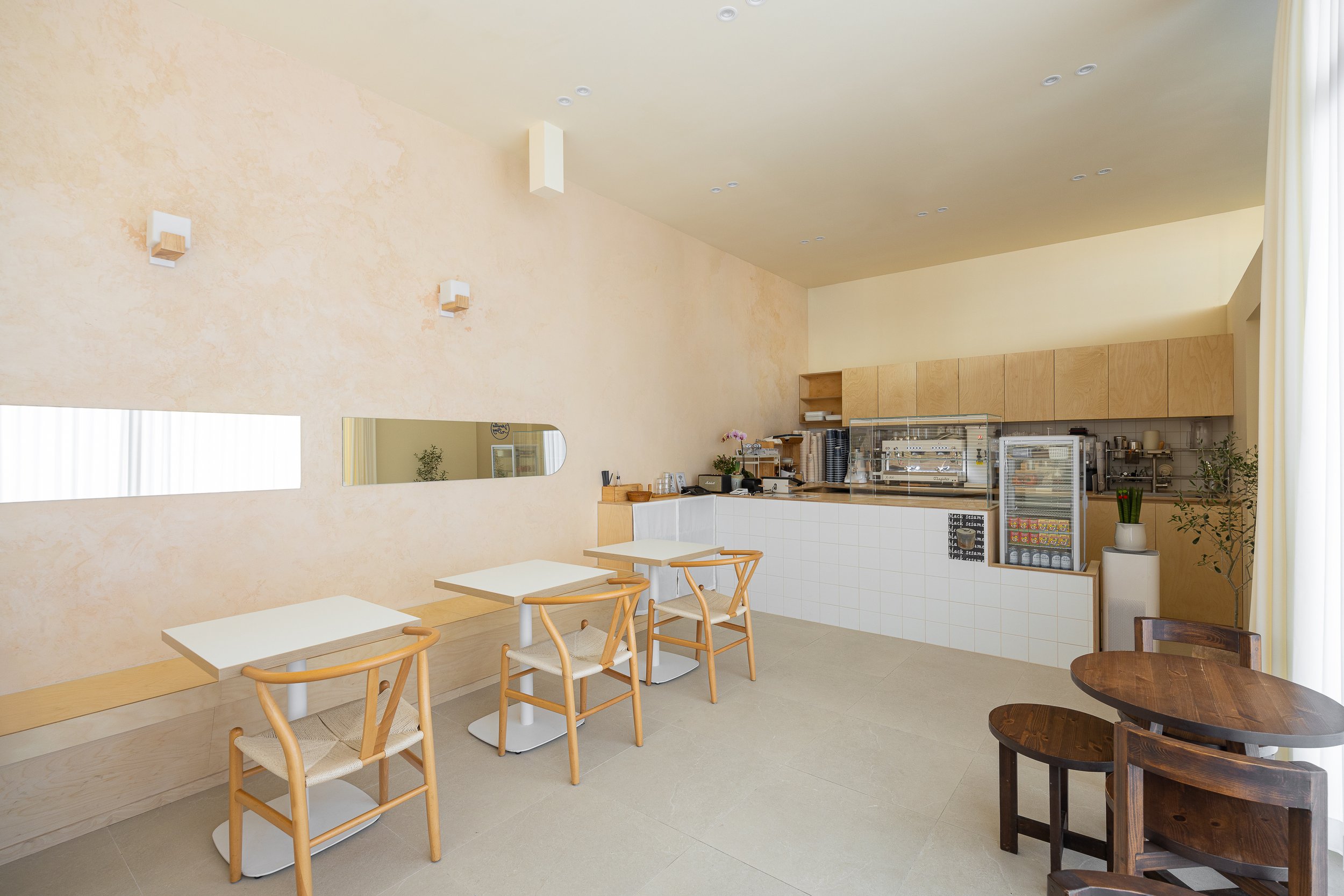 Minimalist cafe interior with light wood furniture, white walls, and cafe equipment.