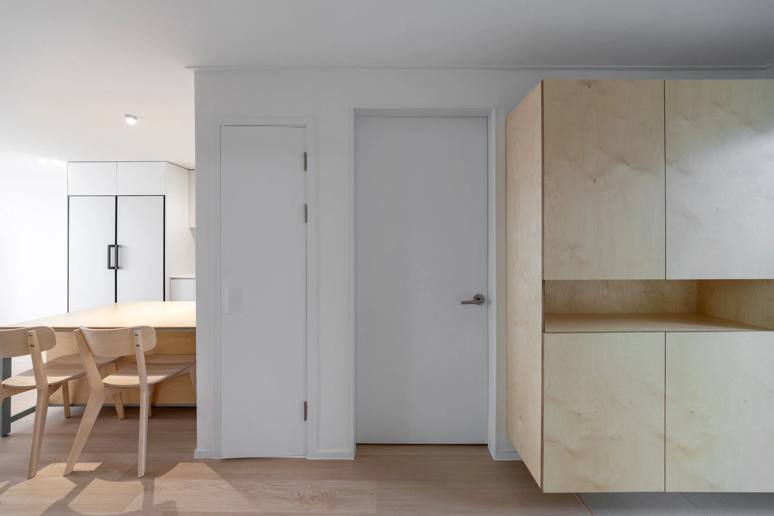 Indoor scene with white doors, wooden cabinets, and light wood dining table with chairs.