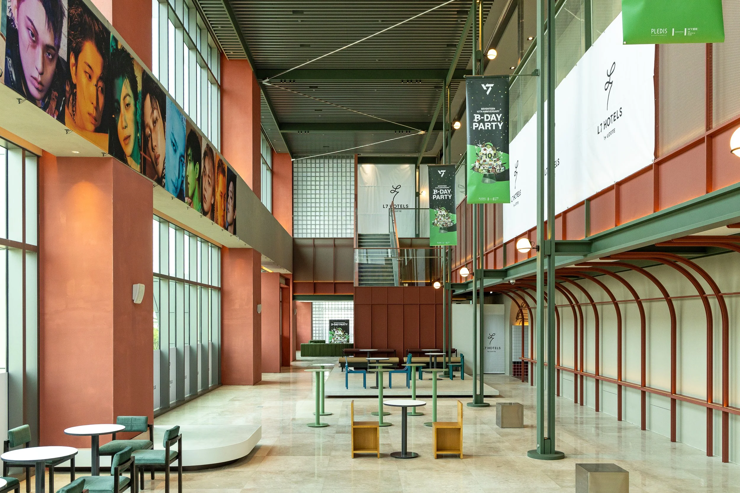 Modern hotel lobby with high ceilings, colorful walls, large windows, and promotional banners for a birthday party event.