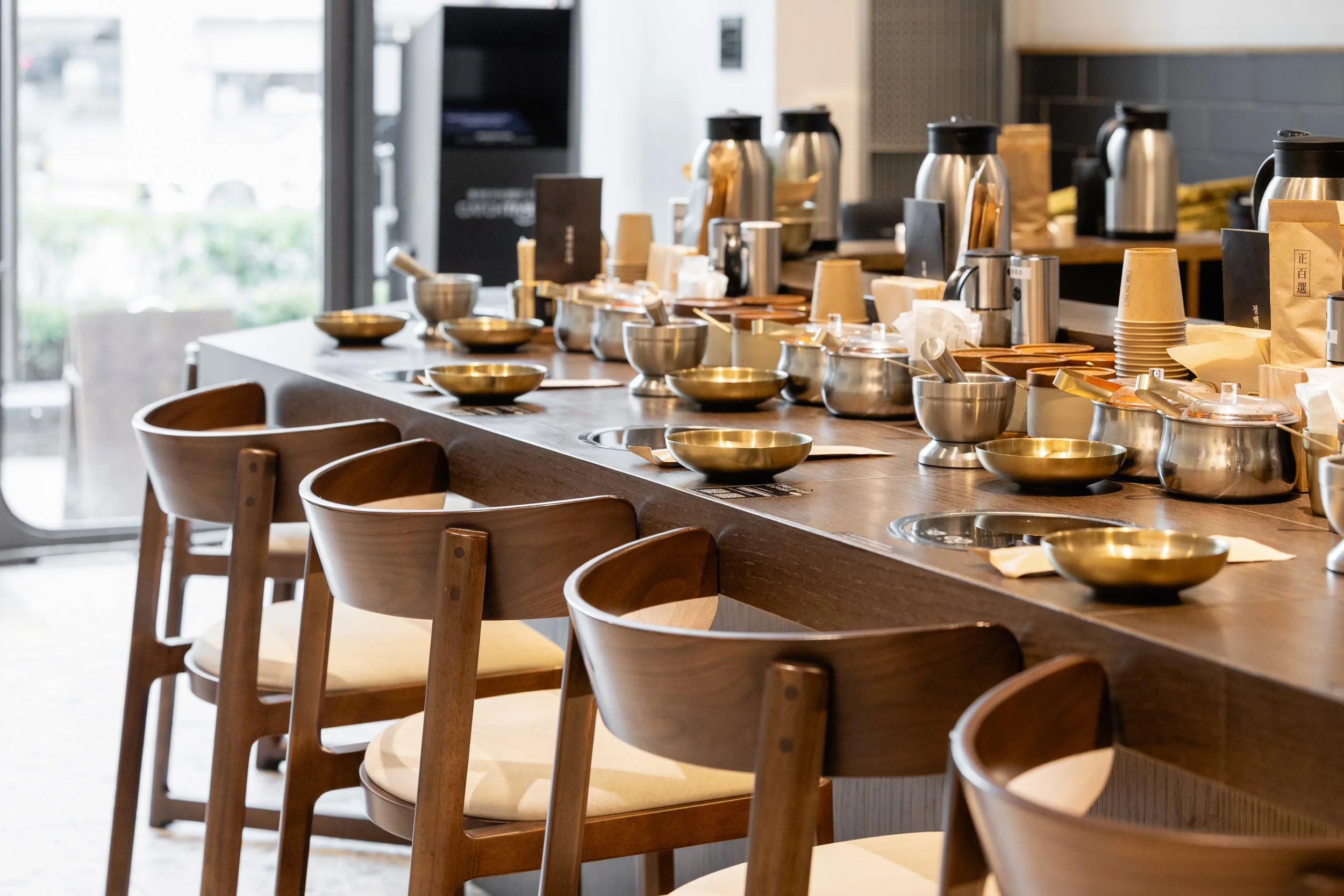 Empty wooden bar stools in front of a counter with bowls, cups, and coffee equipment at a café.