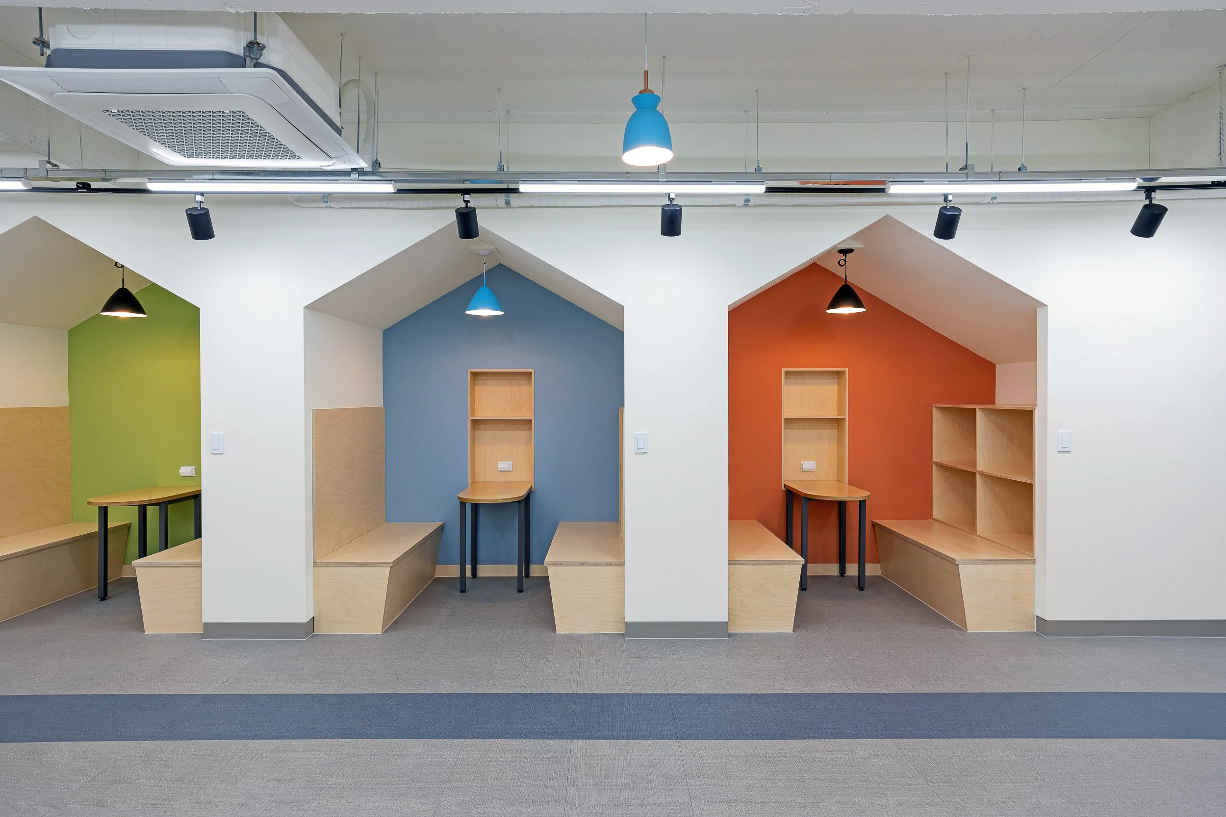 Modern workspace with colorful alcoves, each with a small desk, storage, and hanging lighting.