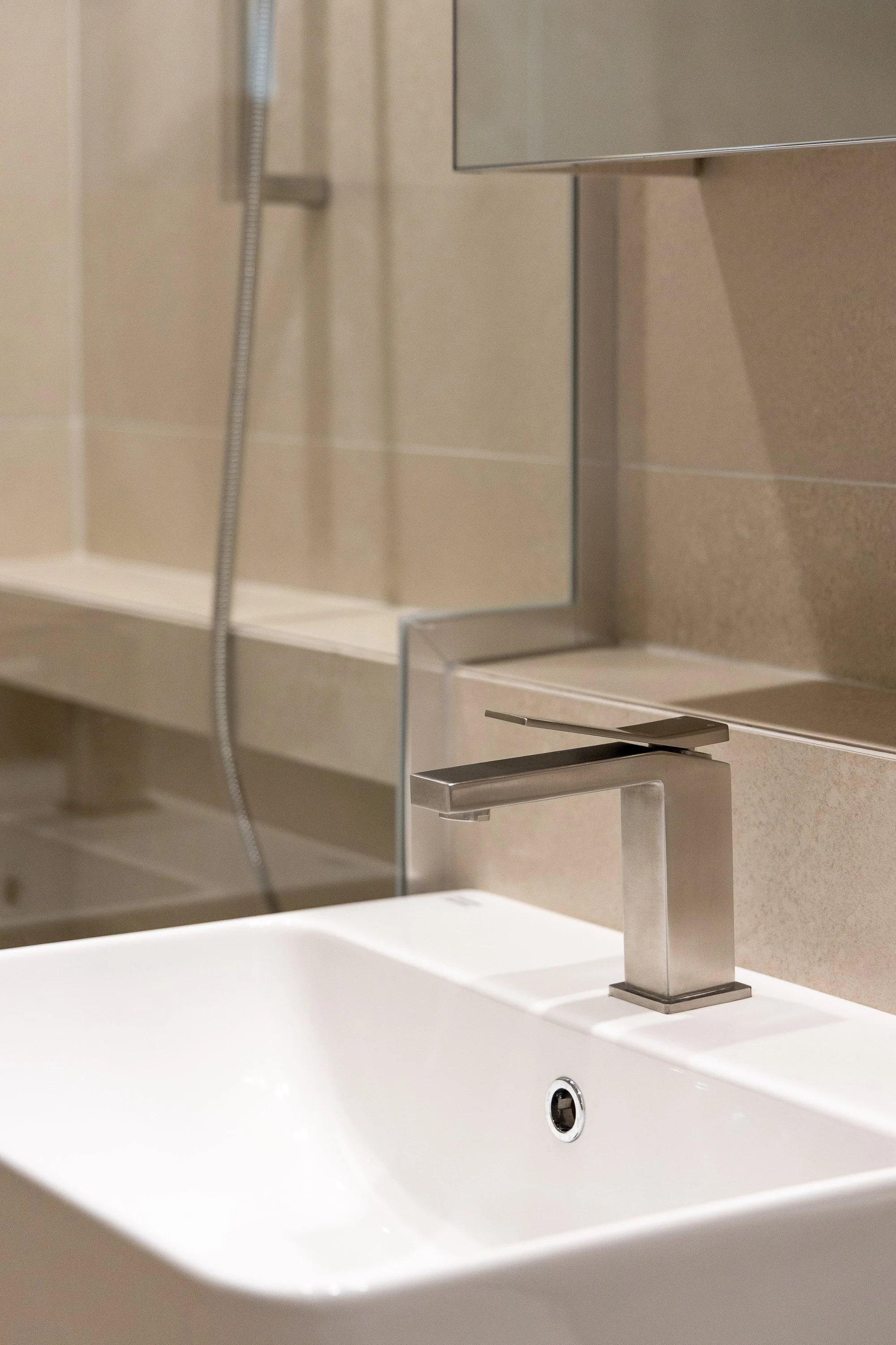 Close-up of a modern bathroom sink with a metal faucet and beige tiled wall.