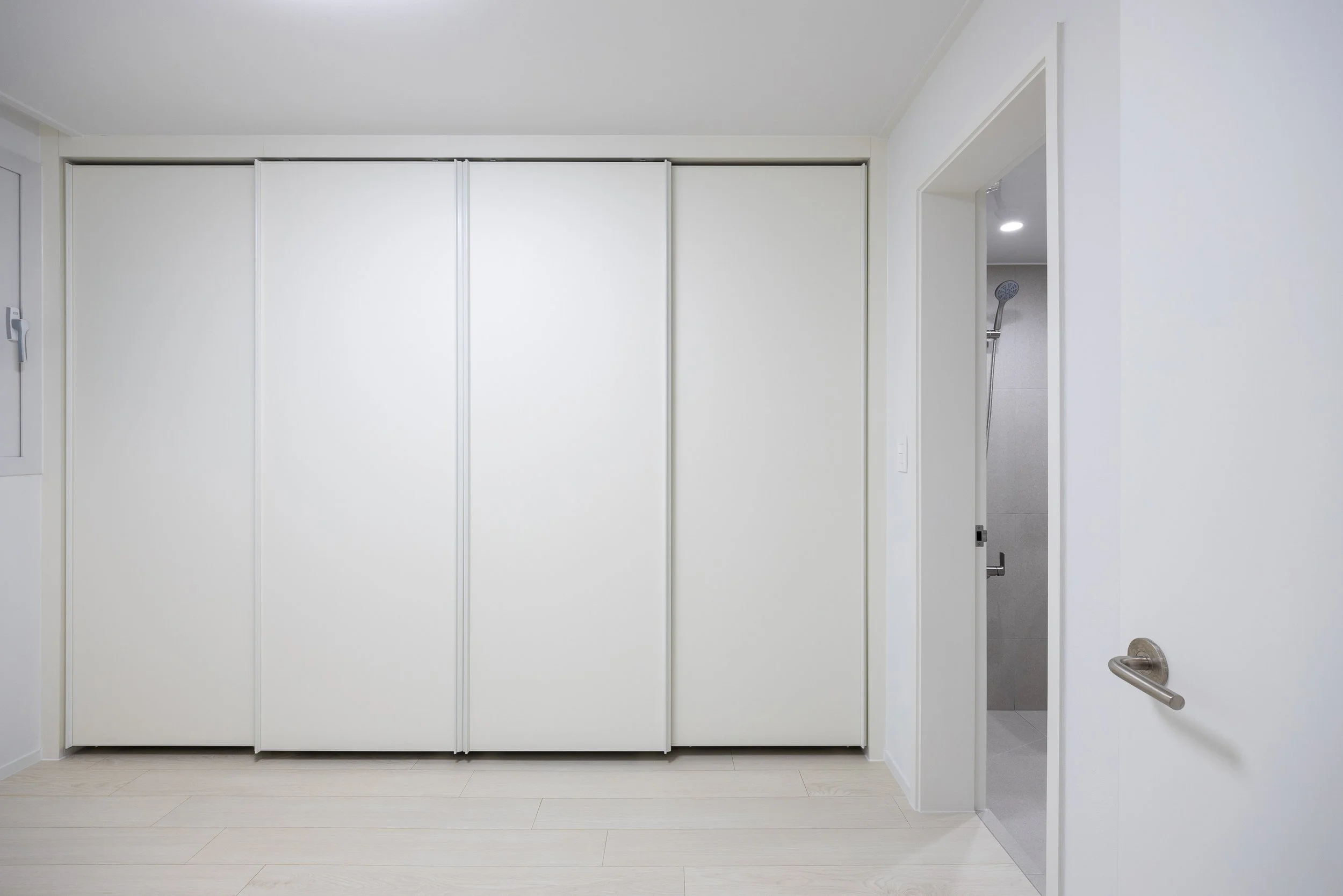 A white closet with sliding doors and a partially open door next to a bathroom with a showerhead visible.