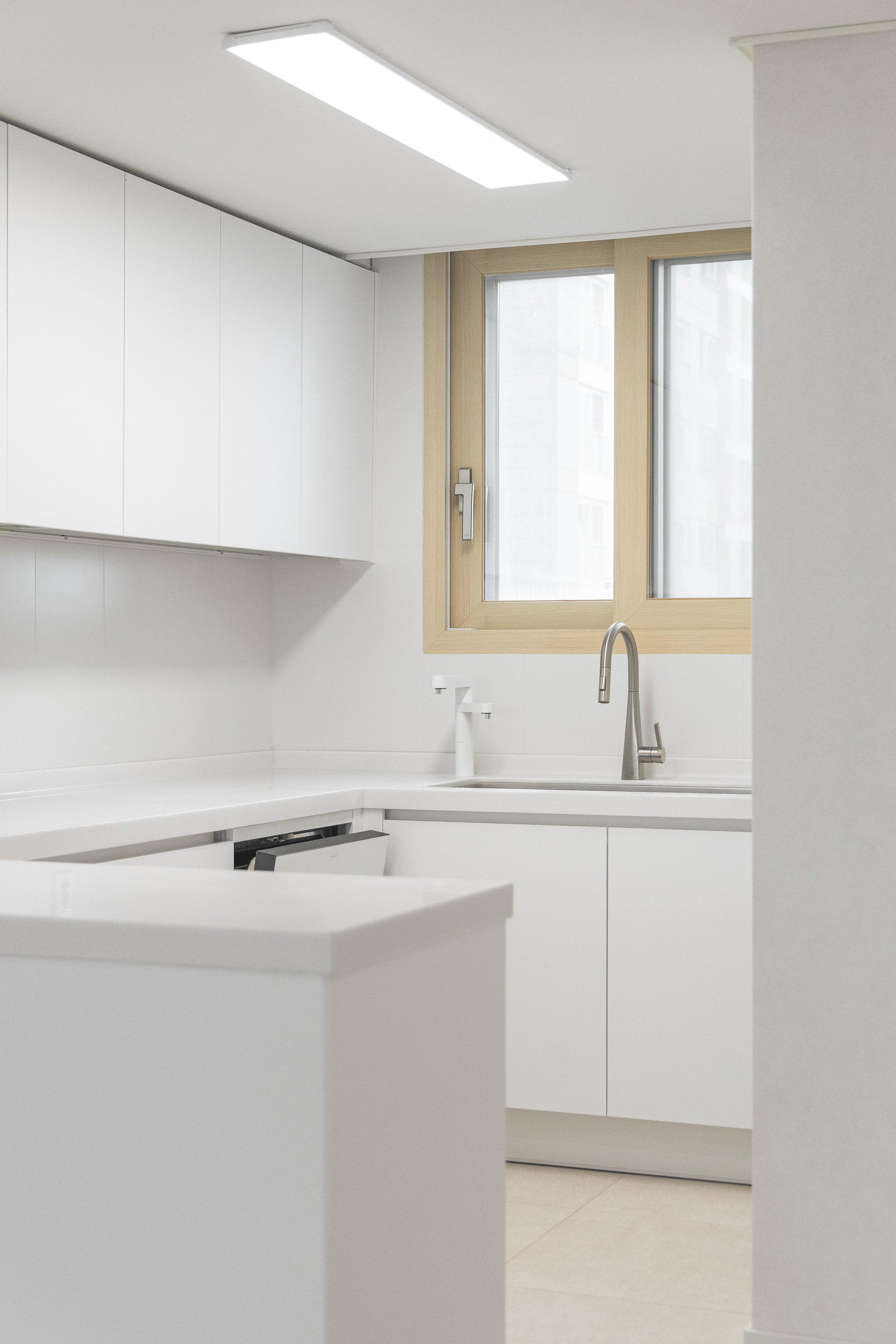 Minimalist white kitchen with a window, sink, and cabinets.