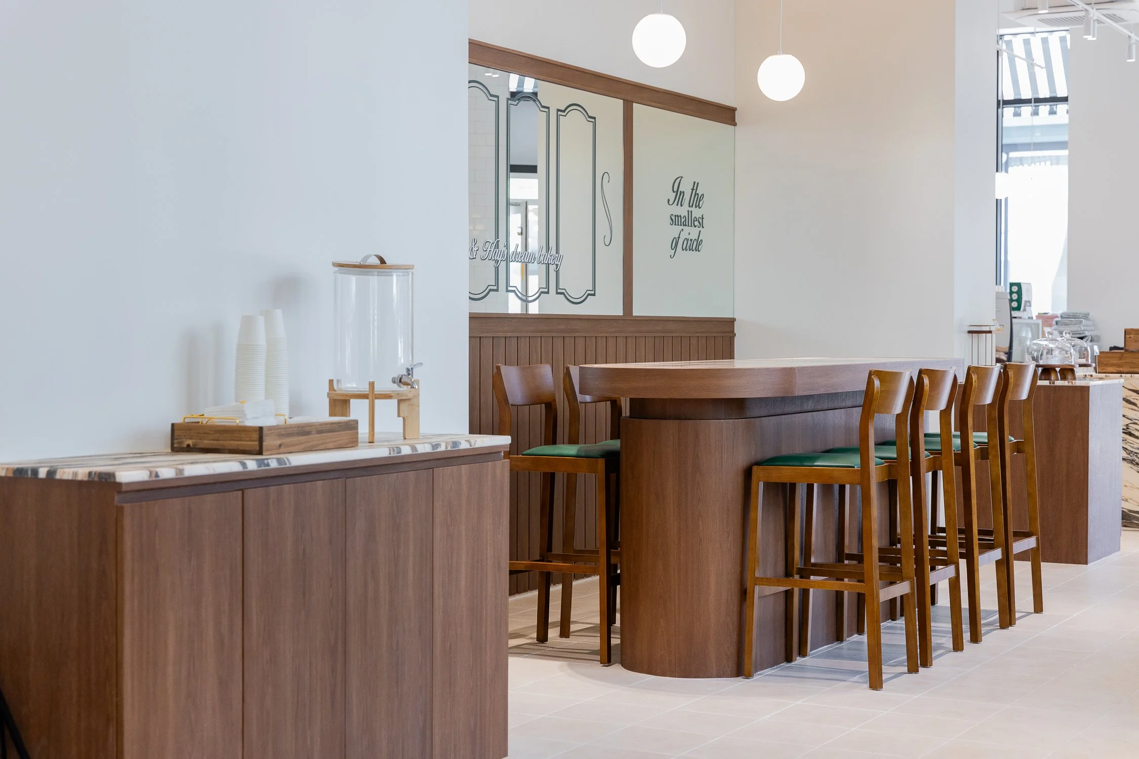Empty cafe with wooden tables and chairs, white walls, and hanging spherical lights.