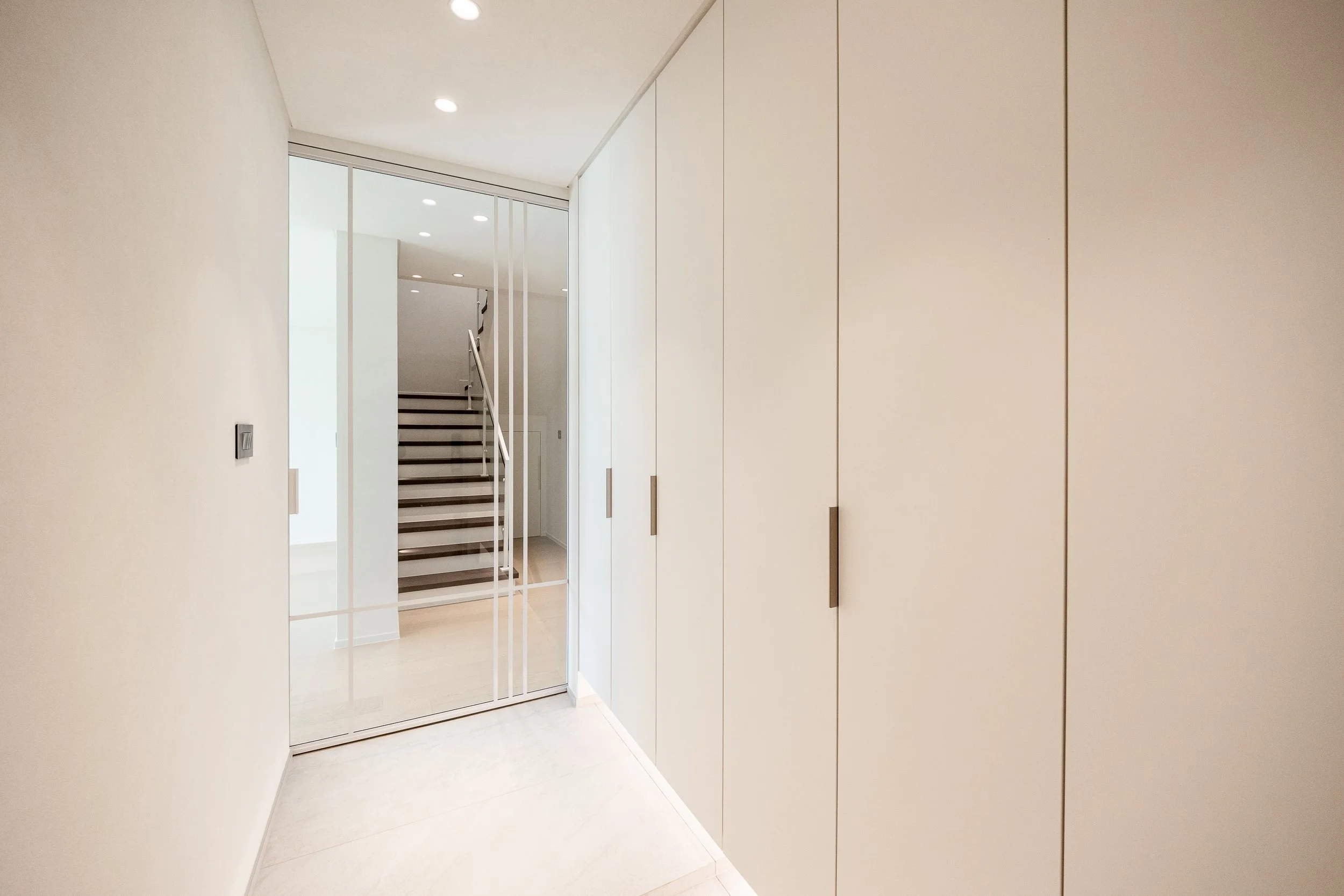 Entrance hallway with built-in white closet cabinets and a glass sliding door leading to staircase.