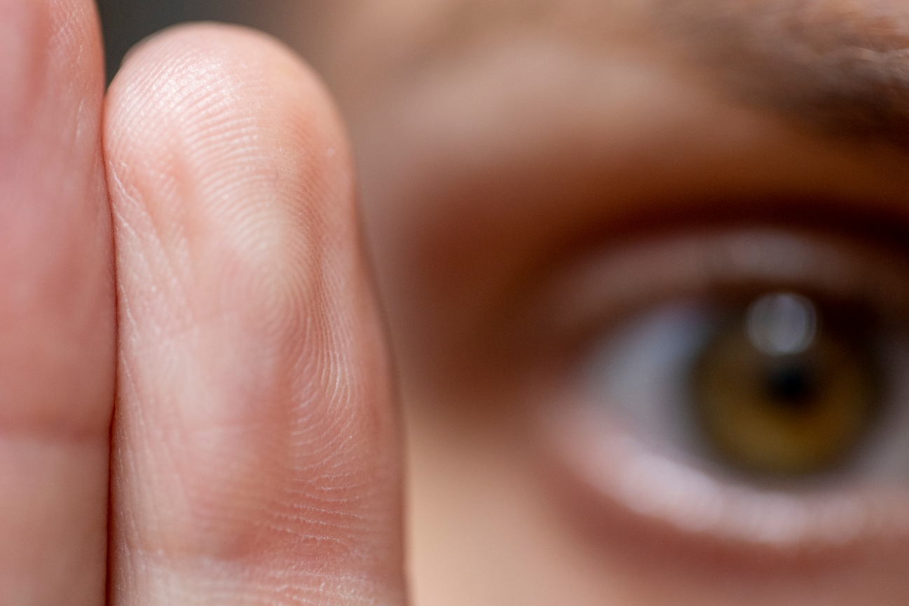 Close-up of a person's eye with the finger partially covering it.