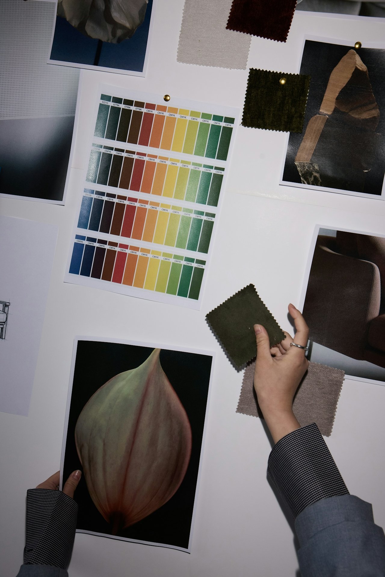 A person looking at fabric samples and color swatches on a table with a printed photo of a plant seed pod, color charts, fabric swatches, and photographs of textures and materials.