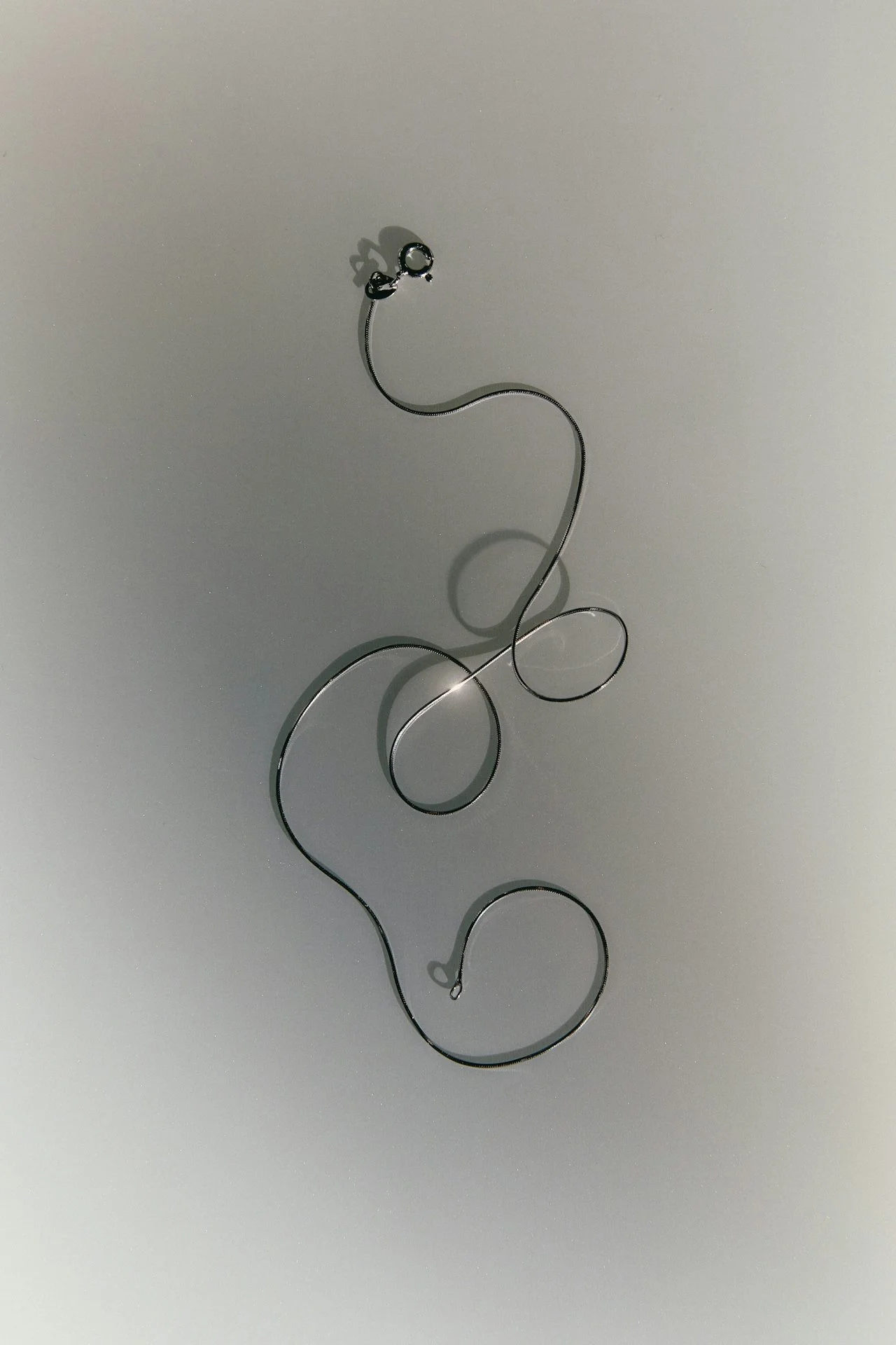 Abstract metal sculpture with loops and curves casting shadows on a plain background.