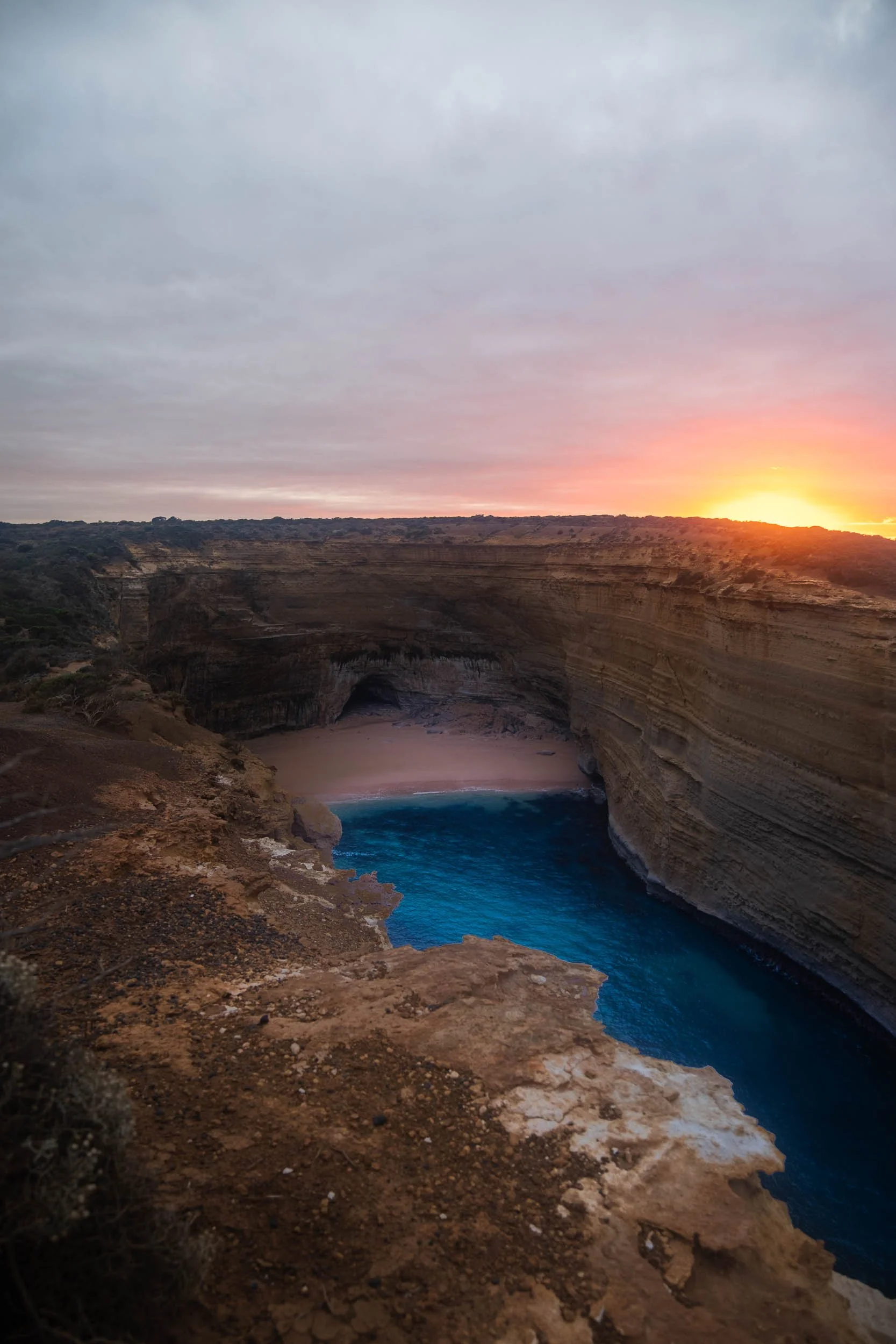 Sunset over a canyon with layered rock walls and a small beach area with blue water in the canyon floor.