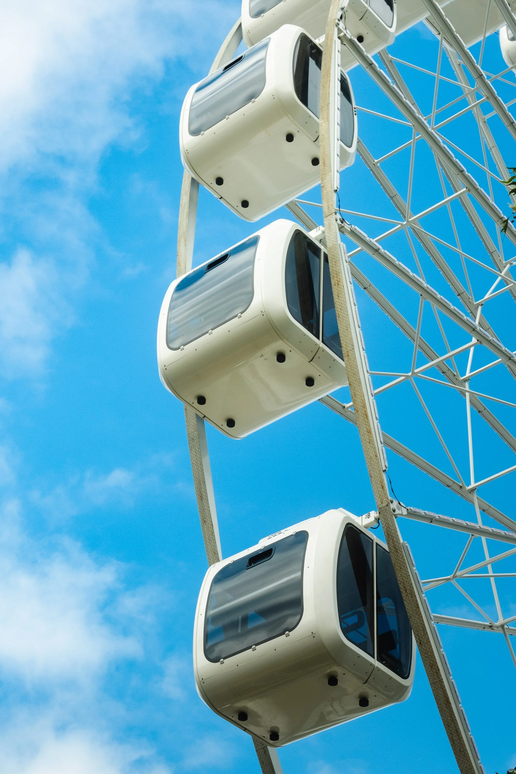 Close-up of three white Ferris wheel cabins against a blue sky with some clouds.
