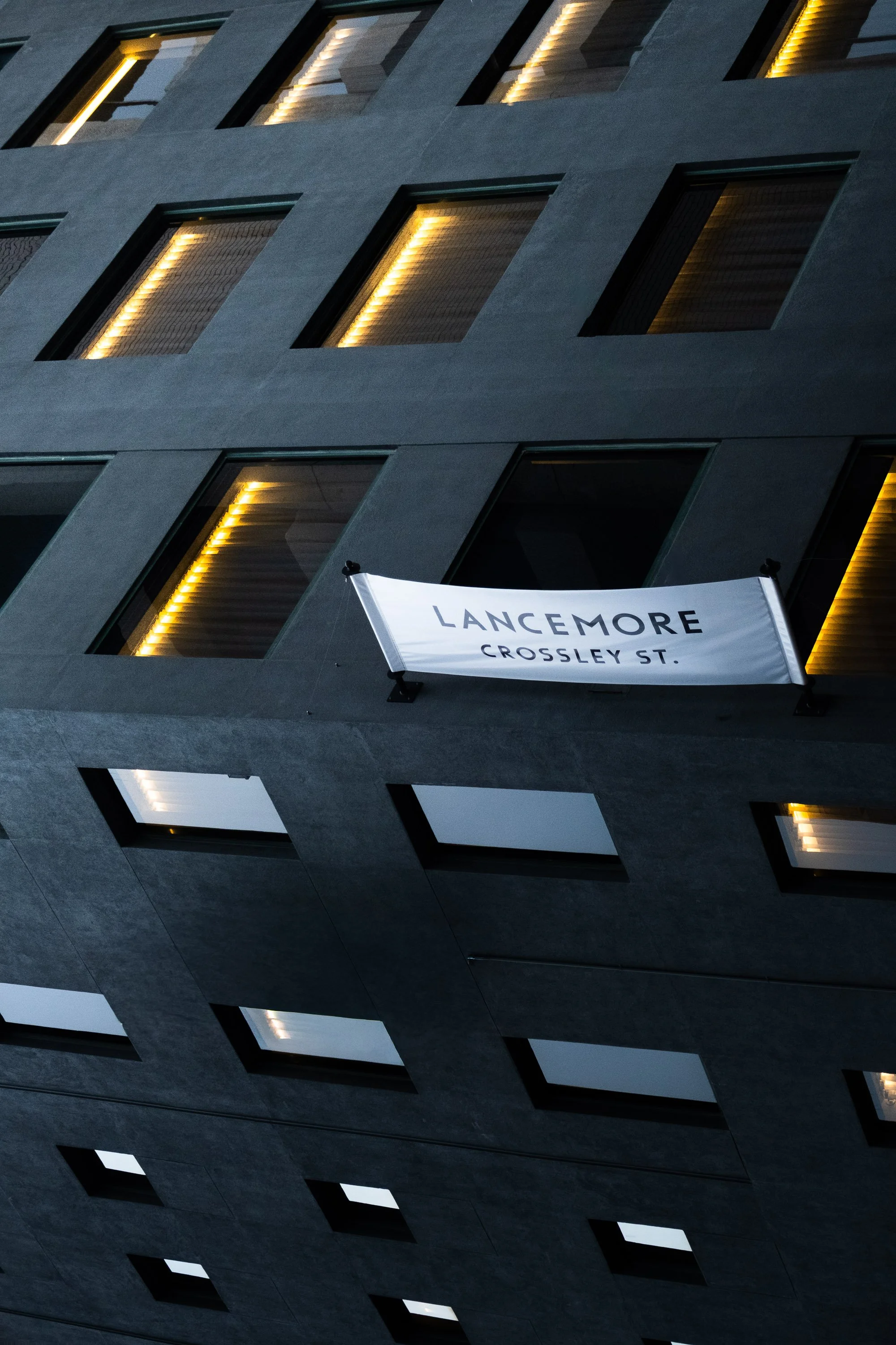 A modern building with illuminated windows and a white banner that reads 'LANCEMORE CROSSLEY ST.'