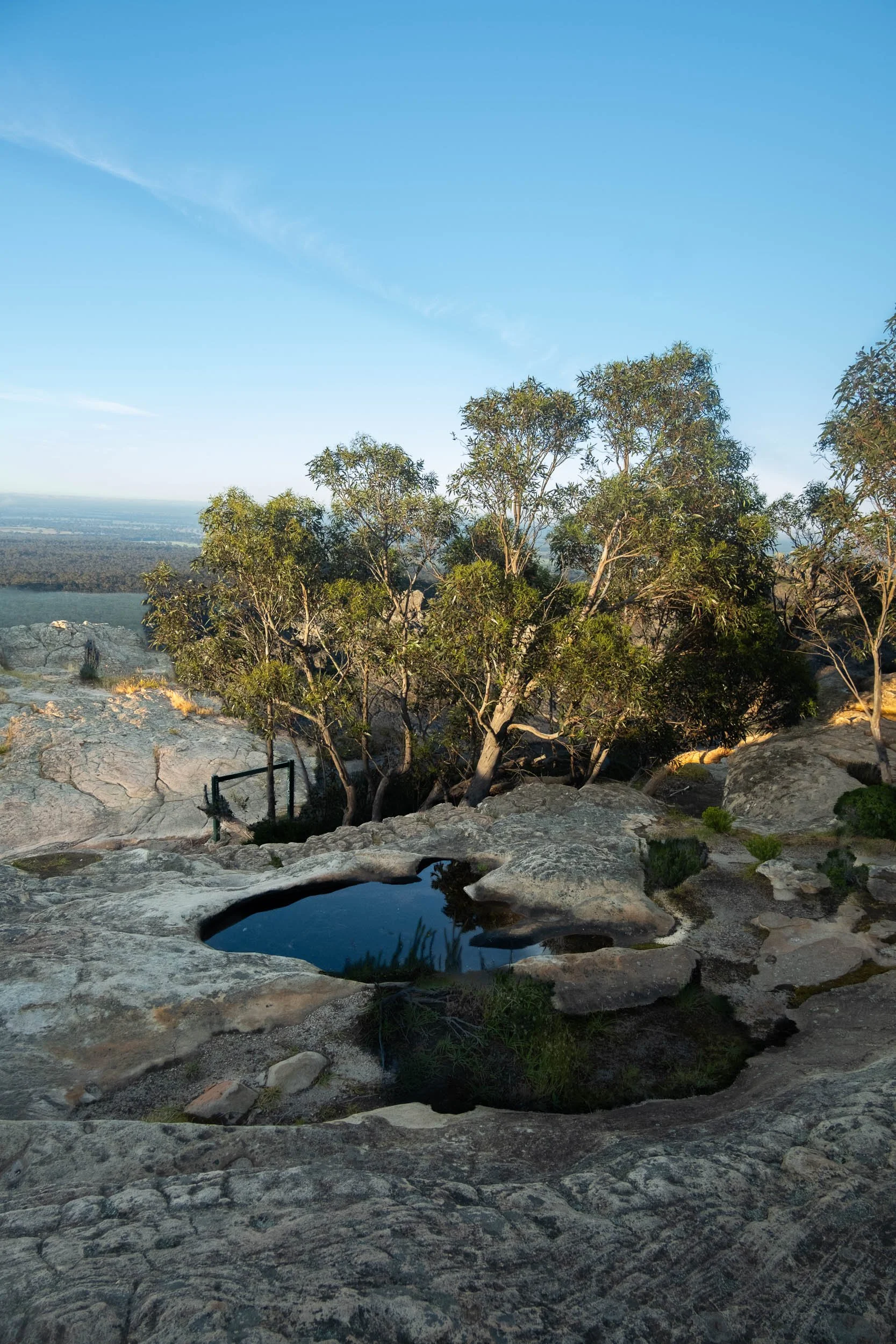 Rocky landscape with a small water pool and trees in the background under a clear blue sky.
