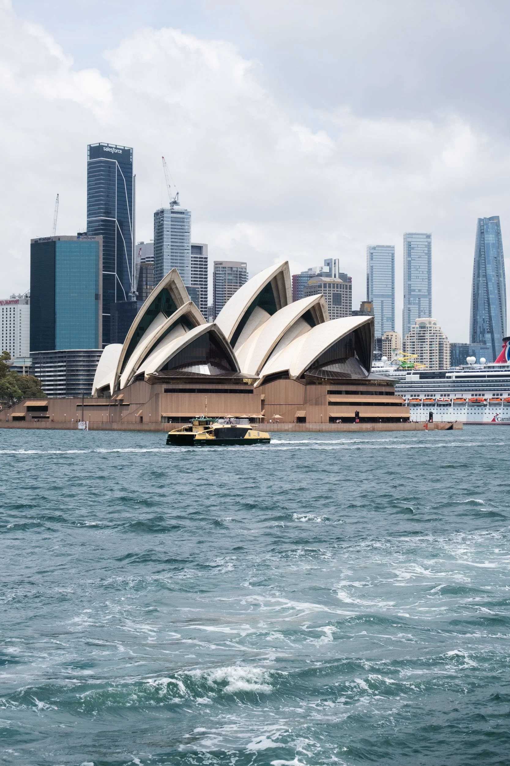 Sydney Opera House with city skyline in the background, seen from the water, with a boat in the foreground.