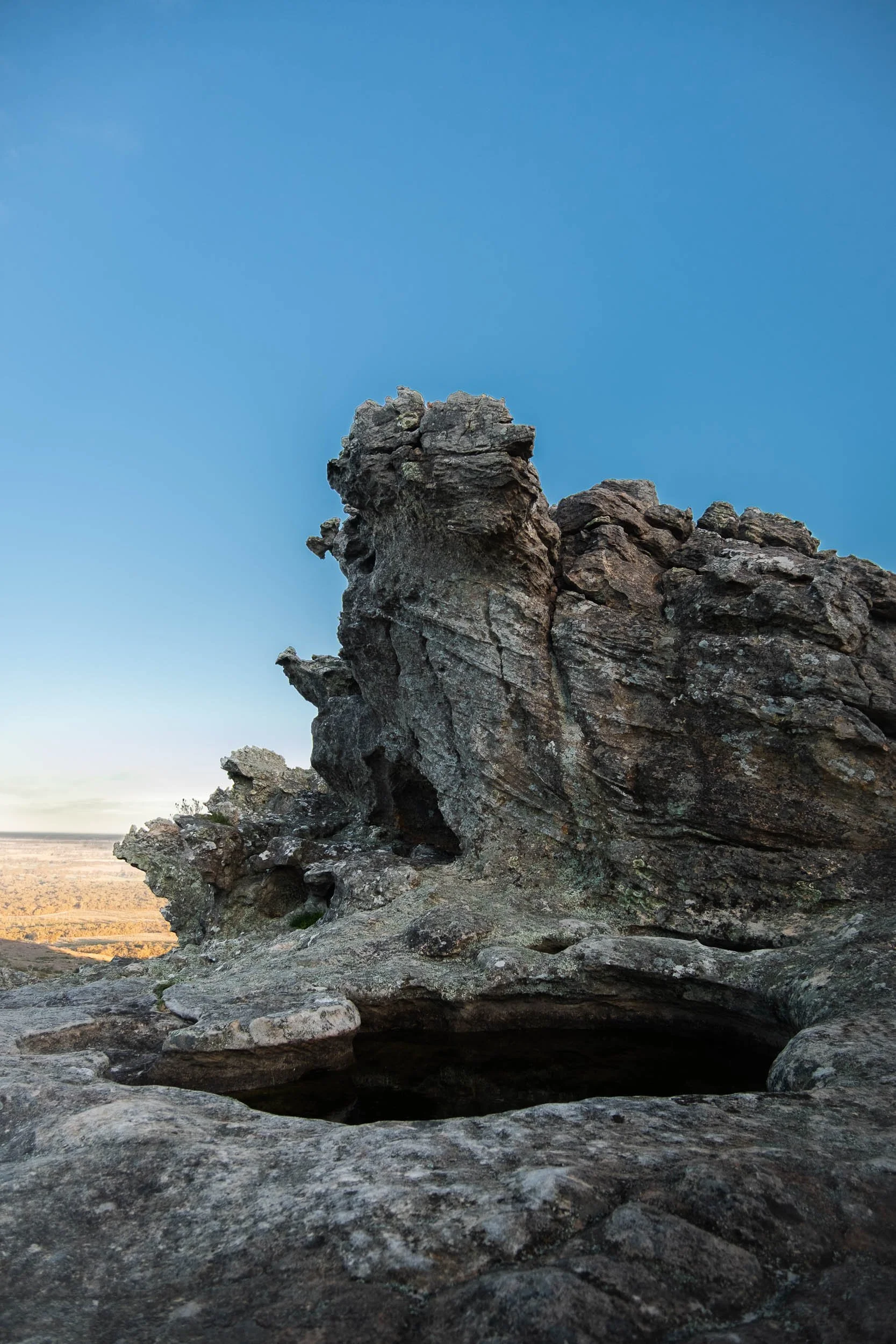 Rugged rock formation against a clear blue sky with a distant landscape visible below.