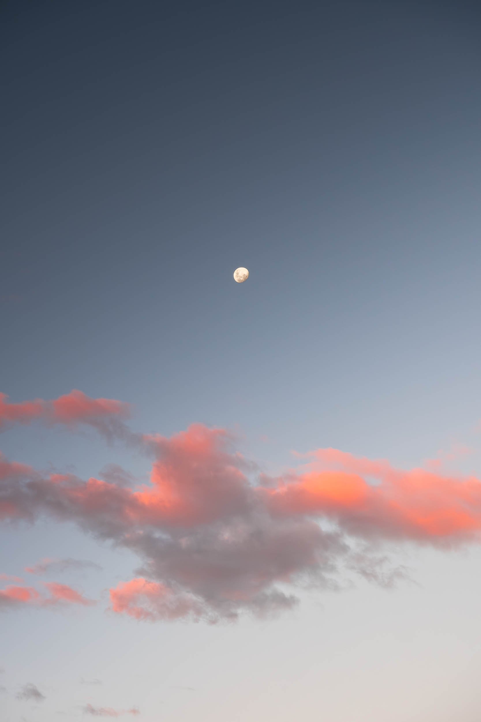 Sky with pink clouds and the moon visible in the early evening or dawn sky.