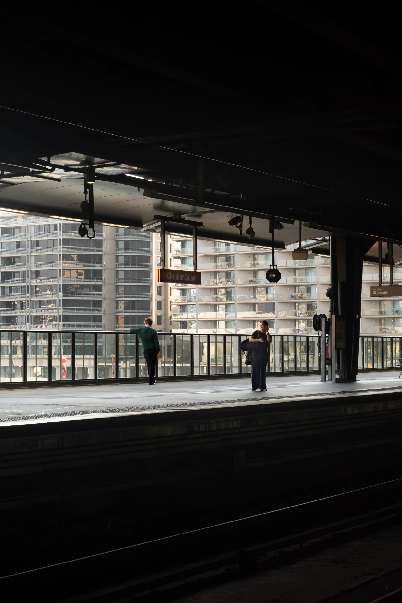 People waiting on an urban train platform with modern apartment buildings in the background.