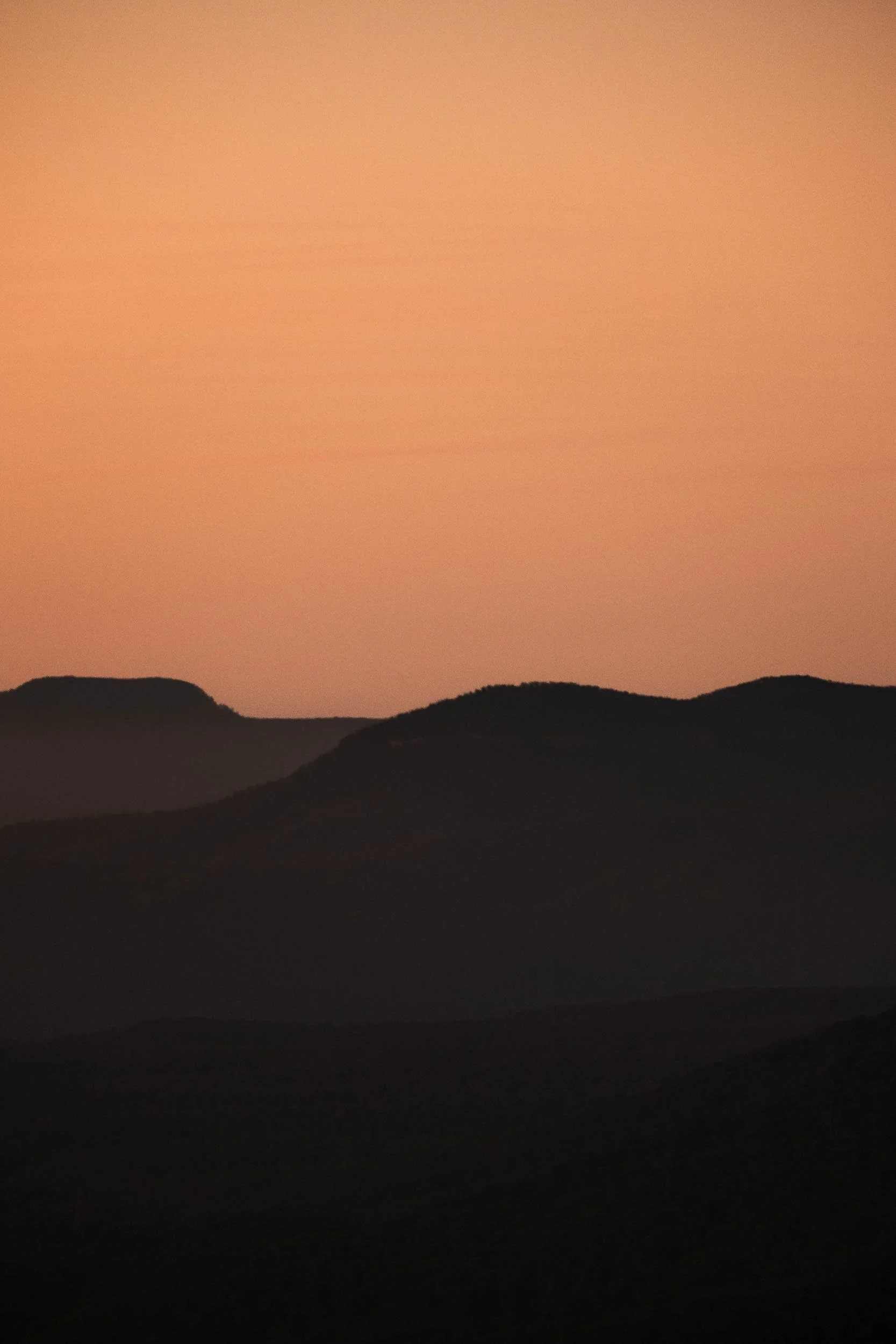 Silhouette of mountains against a pinkish-orange sunset sky.