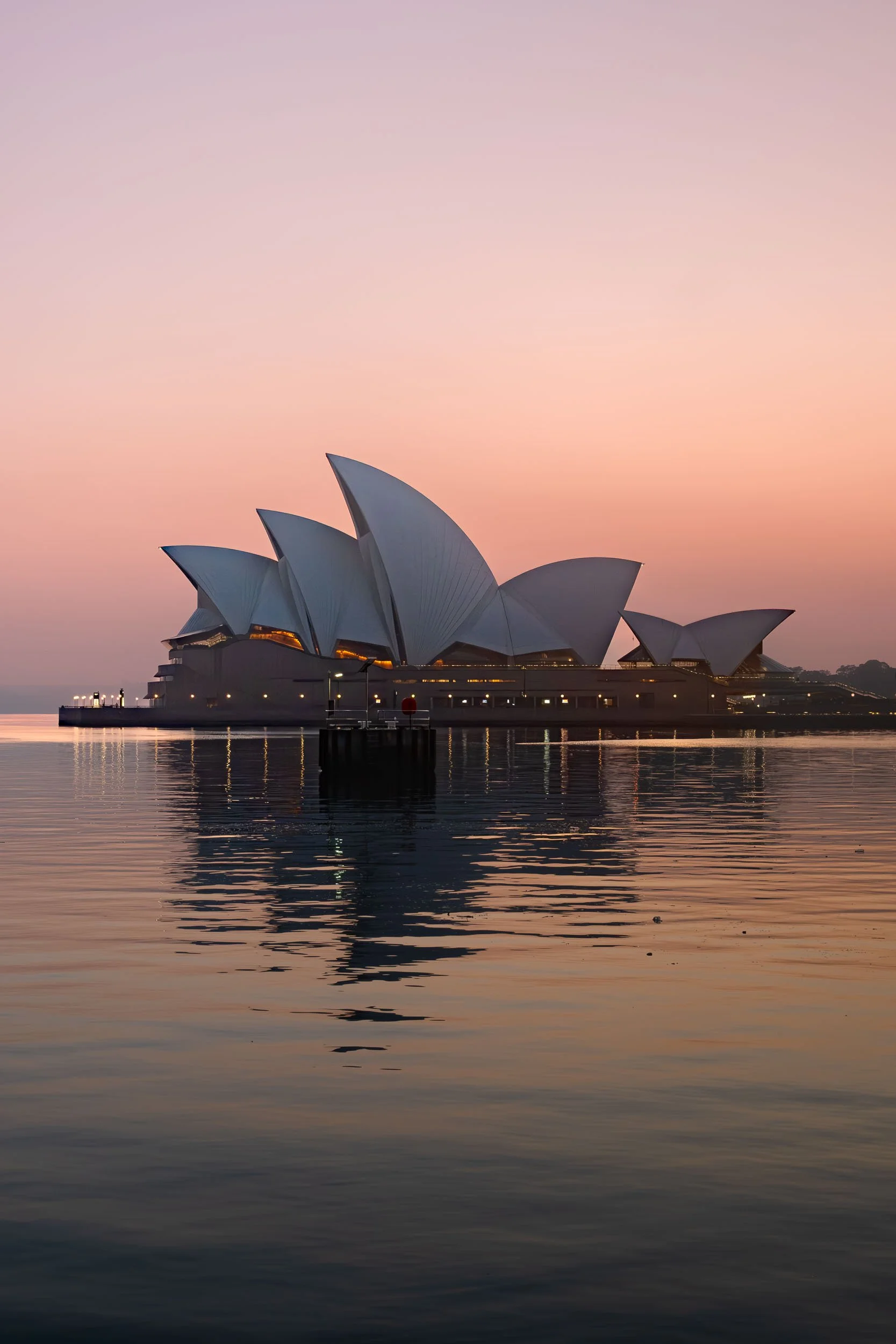 Sydney Opera House at twilight, with a pastel pink and purple sky reflected on the water.