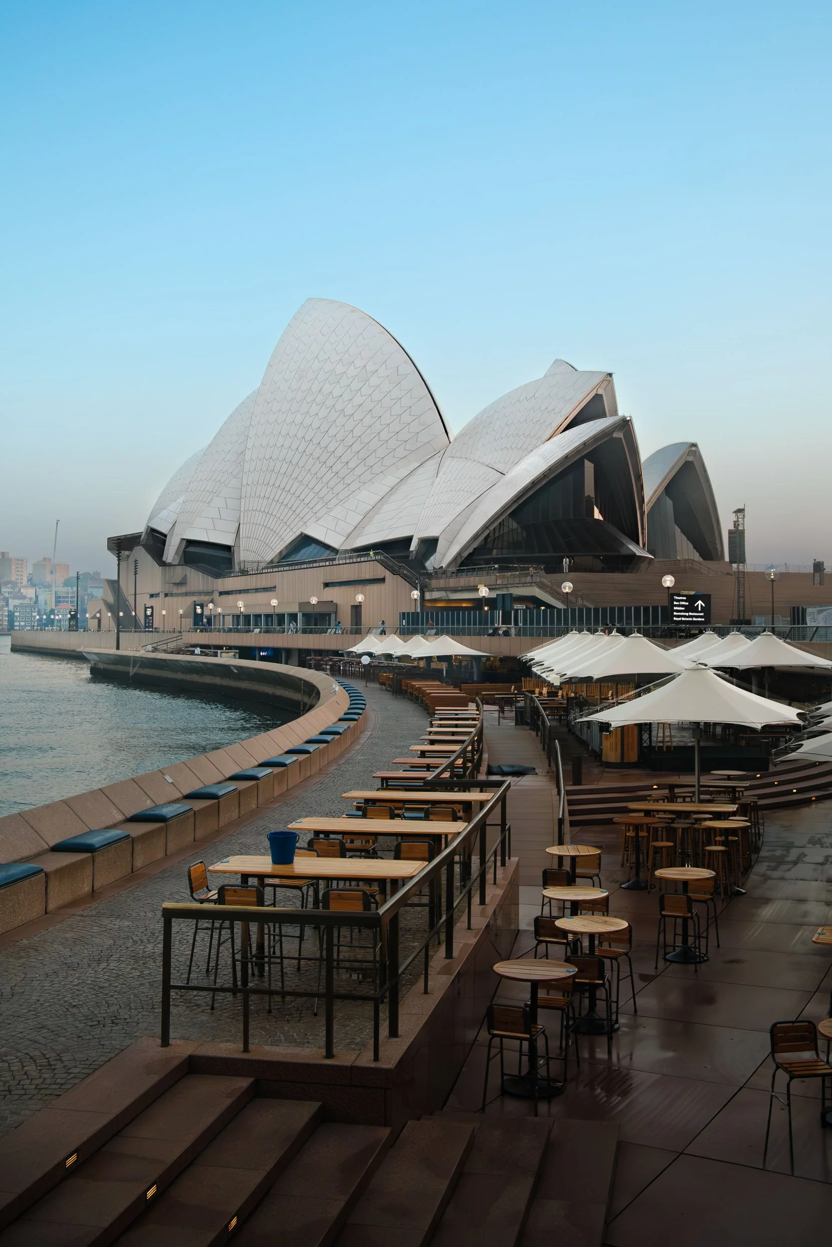 View of the Sydney Opera House with outdoor seating and umbrellas along the waterfront during daytime.