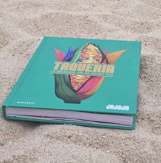 Taquería – Le Mexique en 80 Recettes book resting on sand, featuring Mexican cuisine and contemporary gastronomy, with a mention of mixologist David Paz.