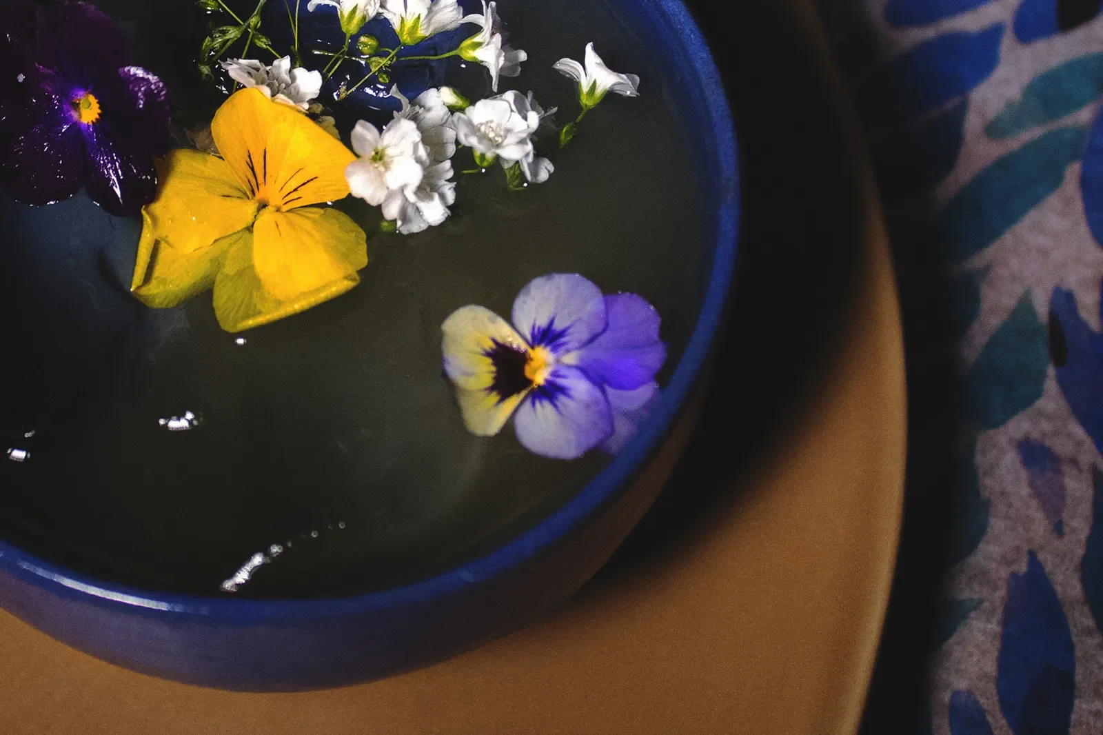 Contemporary author cocktail presented in a blue ceramic bowl, featuring edible flowers and botanical elements, showcasing artistic, high-end mixology design.