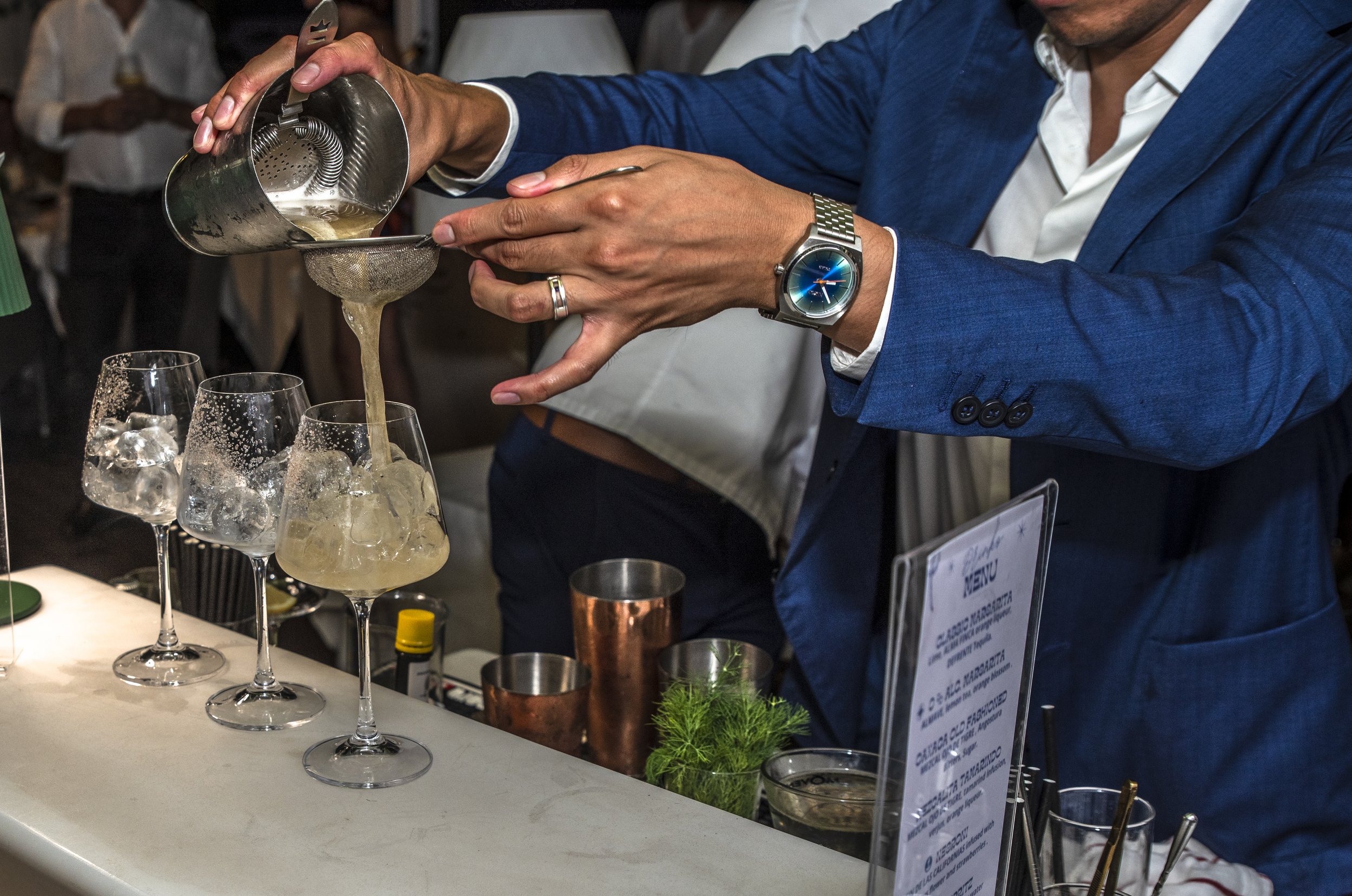 Mixologist David Paz preparing a cocktail during a live bartending event, carefully straining a handcrafted drink into stemmed glasses.