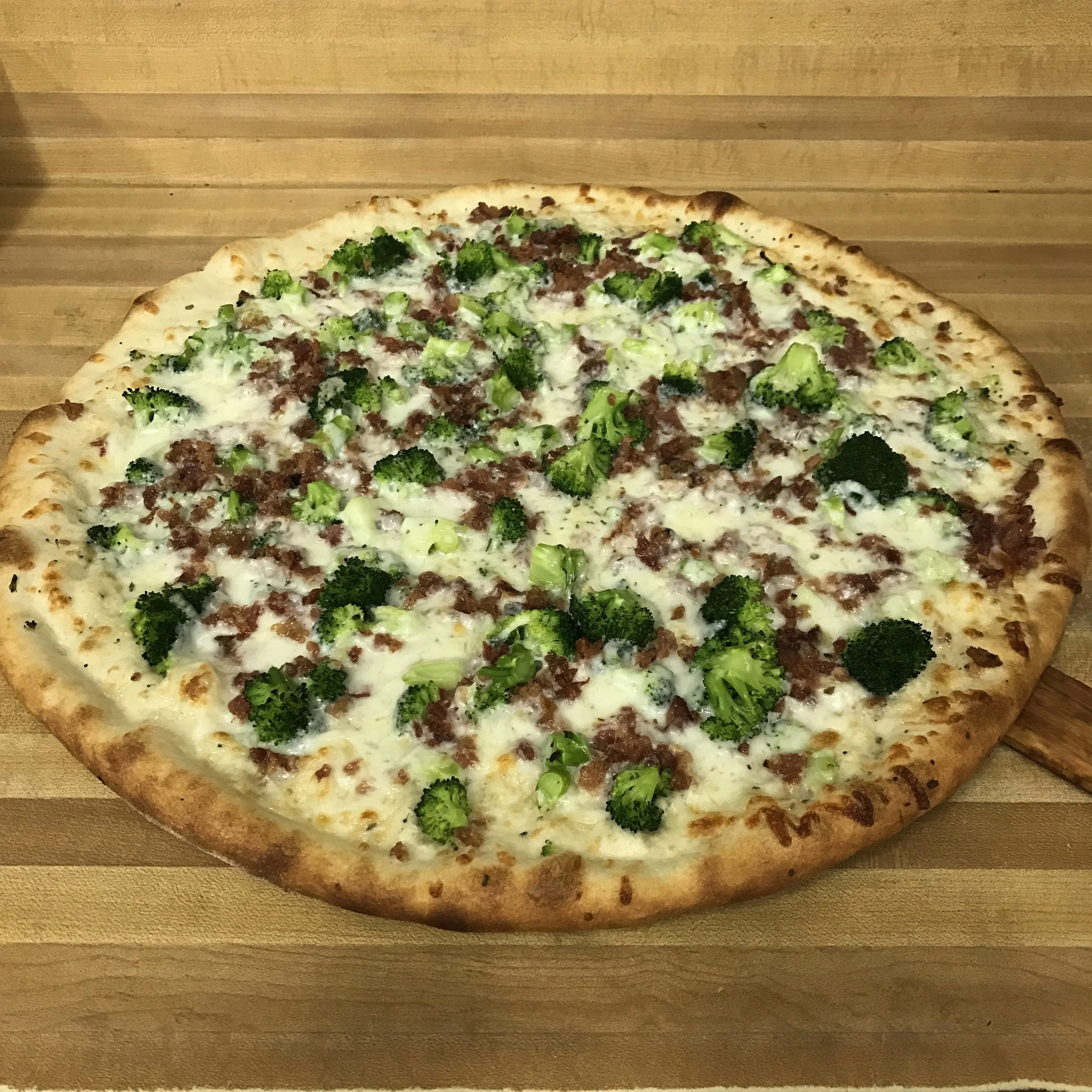A pizza topped with broccoli, ground meat, and cheese on a wooden surface.