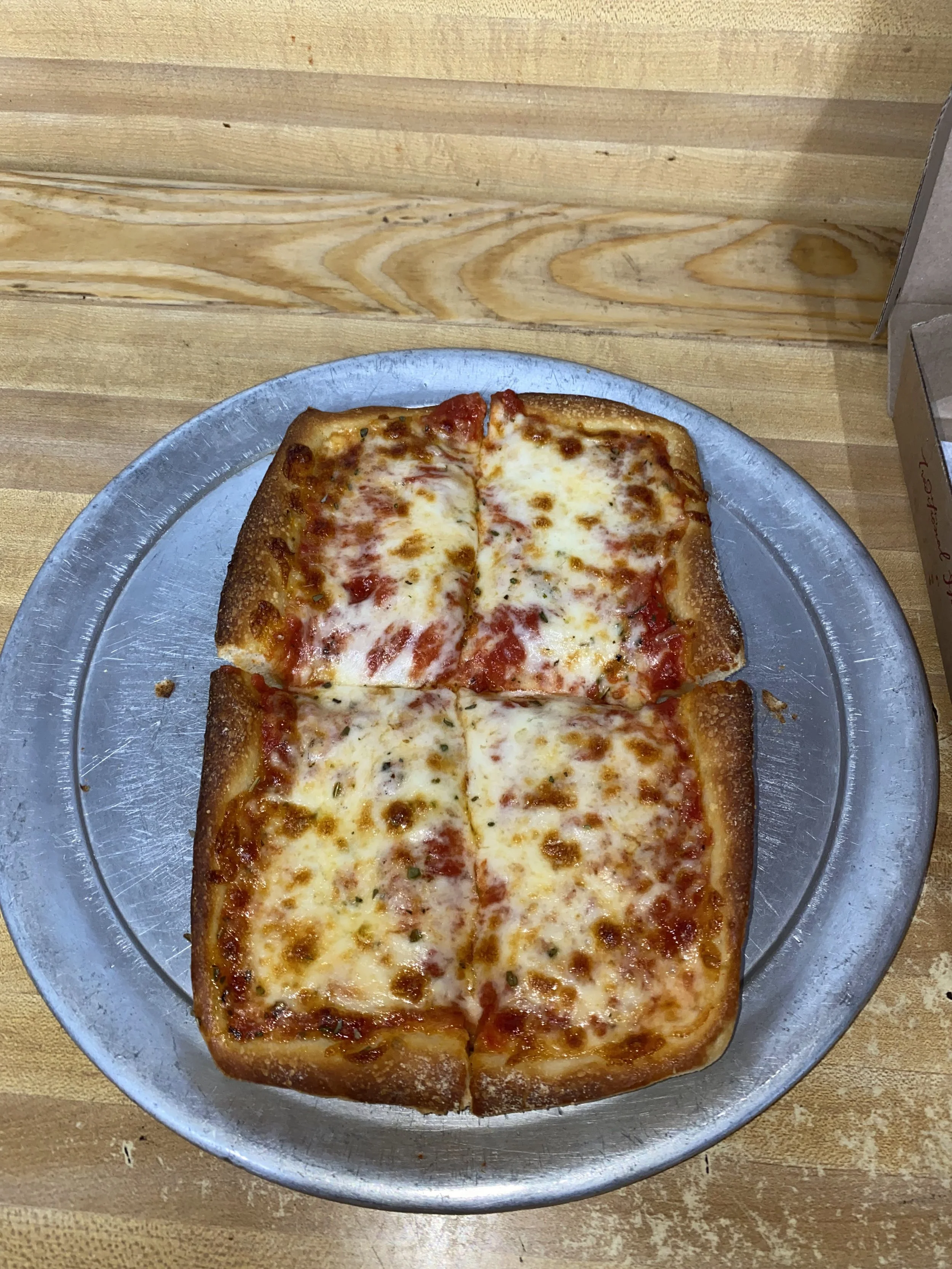 A small rectangular cheese pizza with tomato sauce, baked in a bread-like crust, cut into four slices on a silver tray.