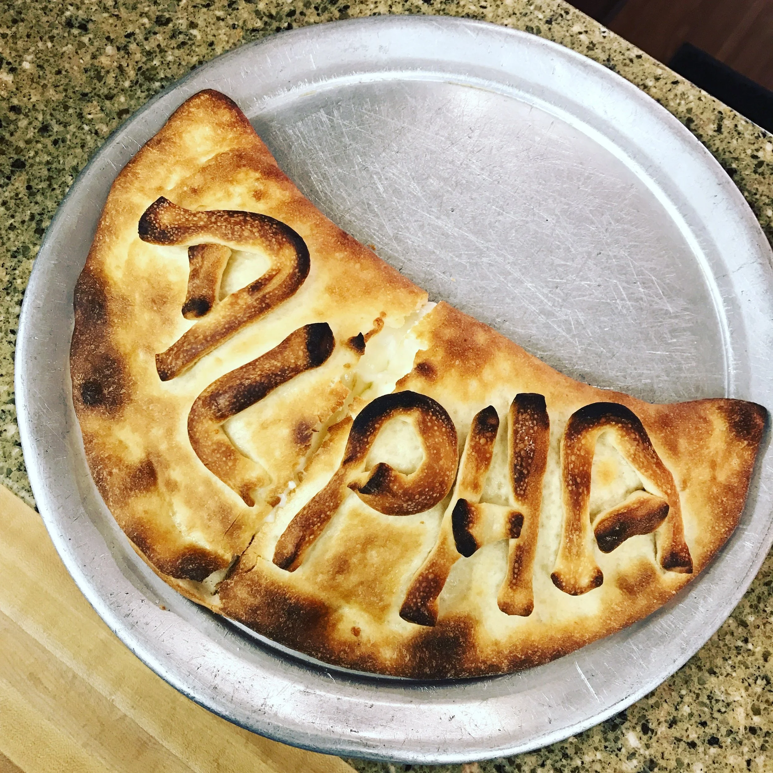 A slice of baked pie with the word 'Thanks' written on it, with slightly burnt edges on a round metal tray.