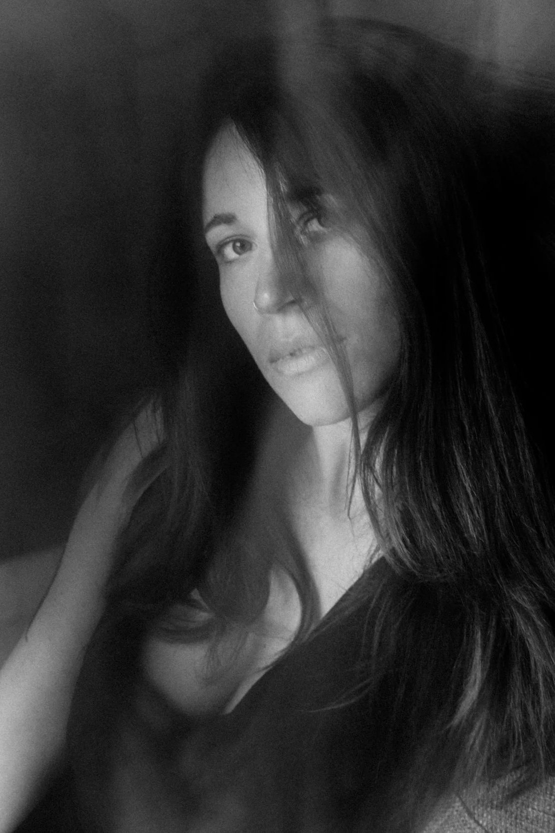 Black and white portrait of a woman with long dark hair, looking at the camera with one eye partially covered by her hair.