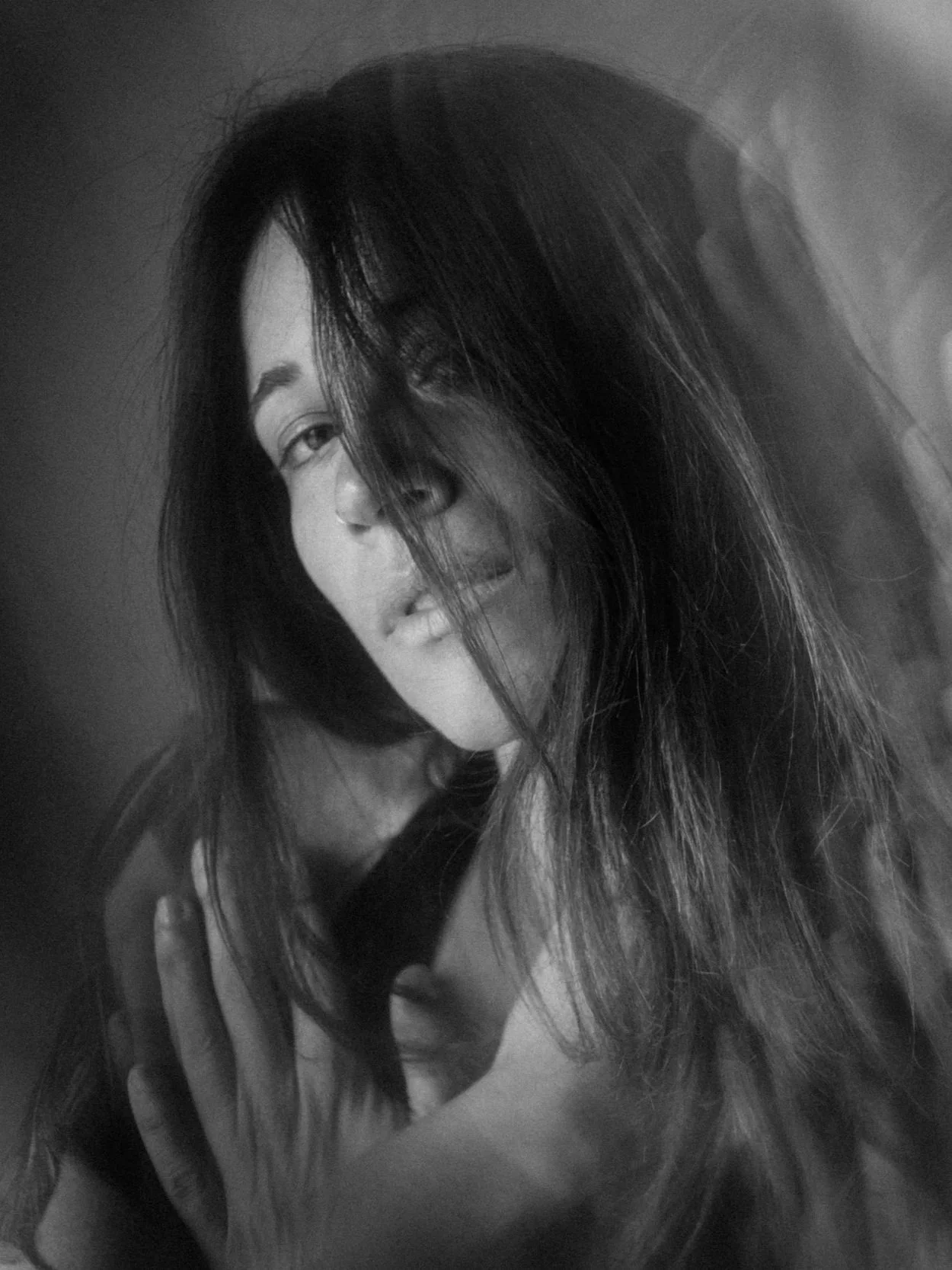 Black and white portrait of a woman with long dark hair partially covering her face, smiling subtly, looking directly at the camera.