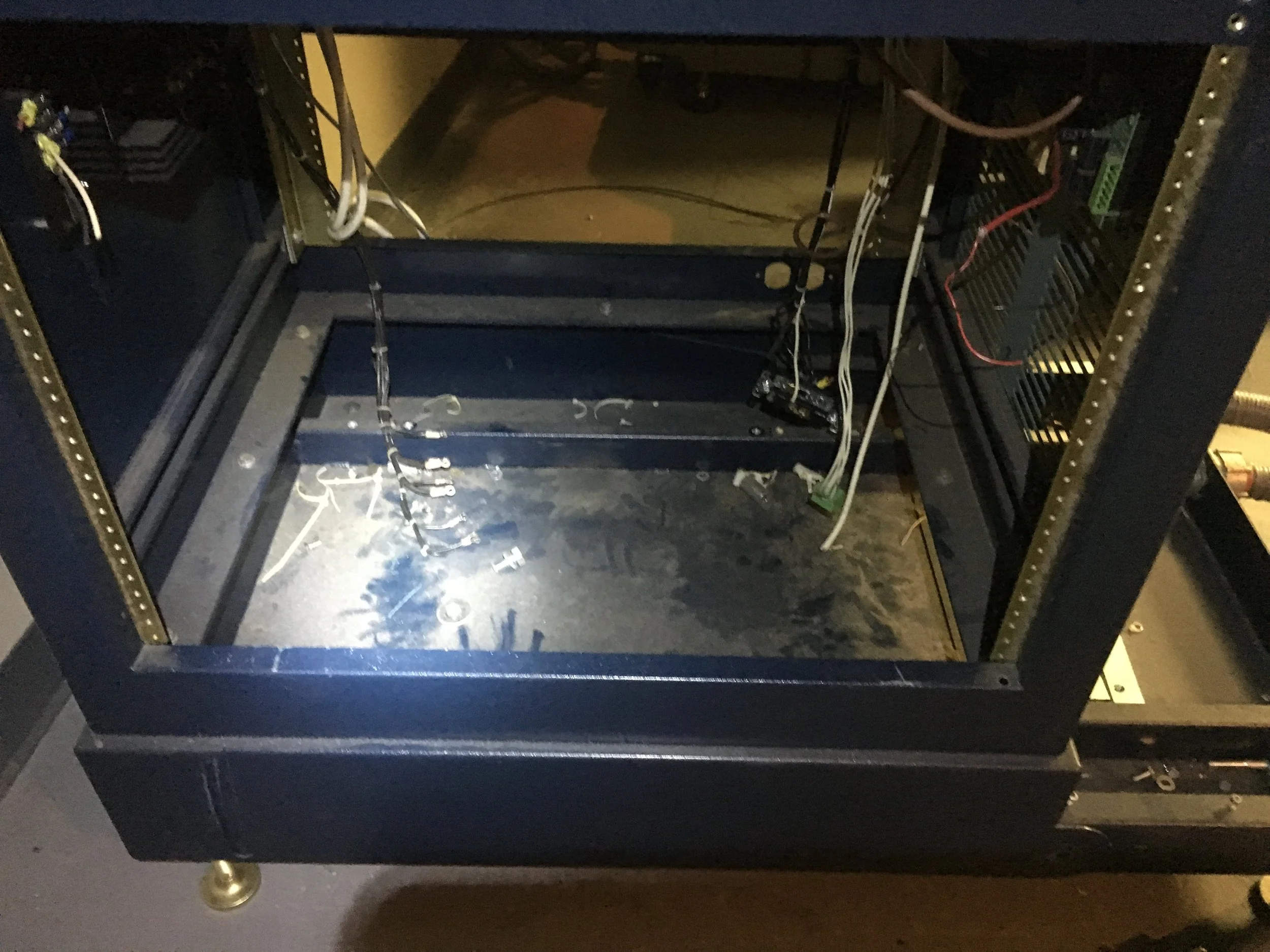 Empty black metal computer case with wiring and components inside, on a gray floor.