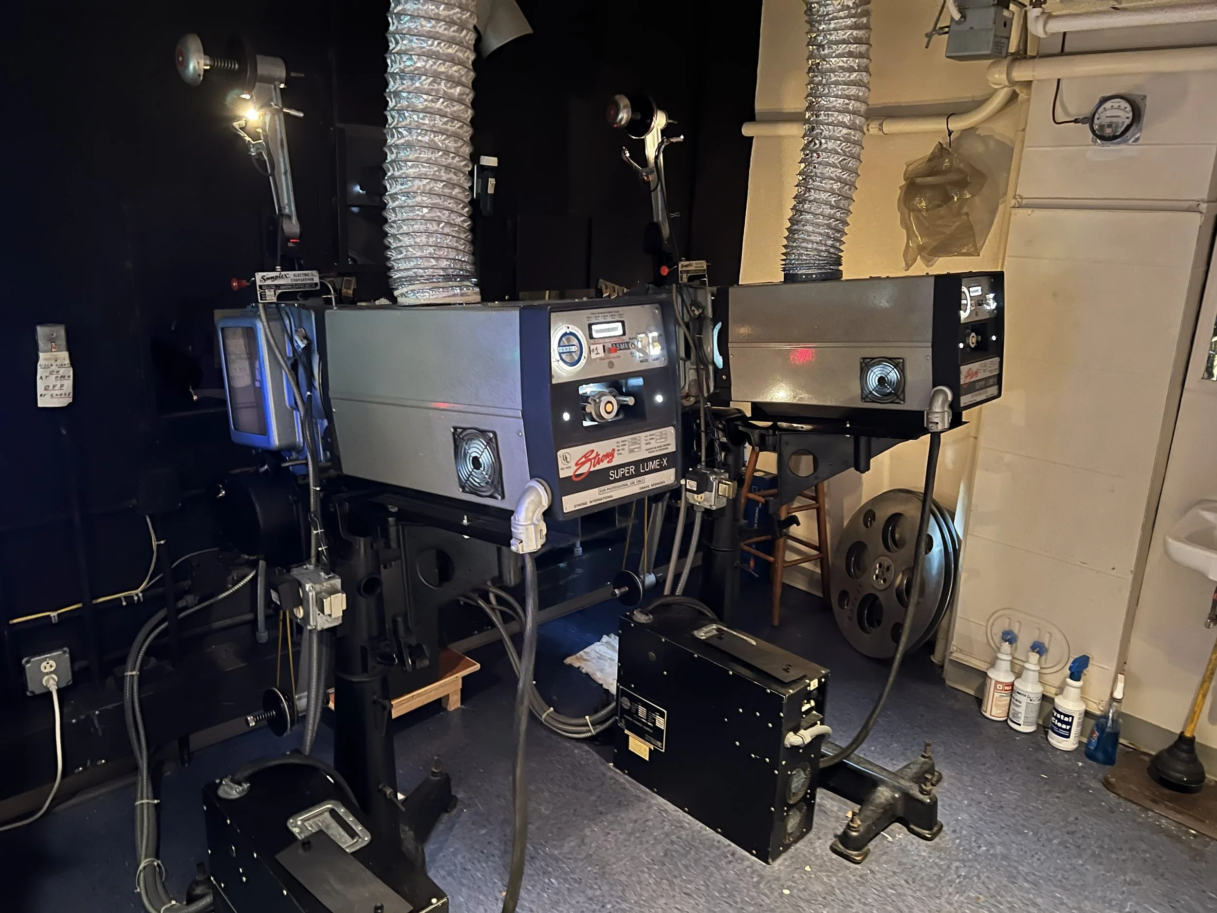 Two industrial laser machines in a workshop with black walls and exposed ductwork, surrounded by various tools and equipment.