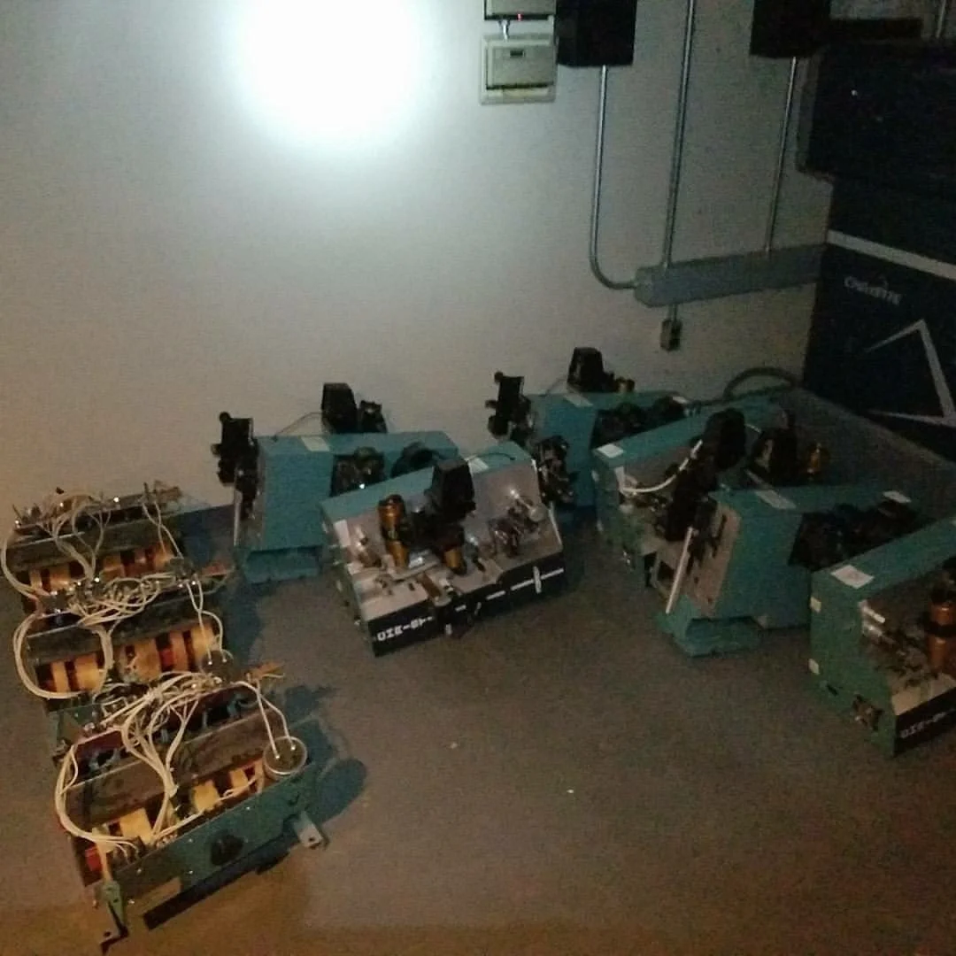 Multiple electronic circuit boards with components and wiring, placed on a dark surface in a room with a white wall and some equipment mounted on the wall.