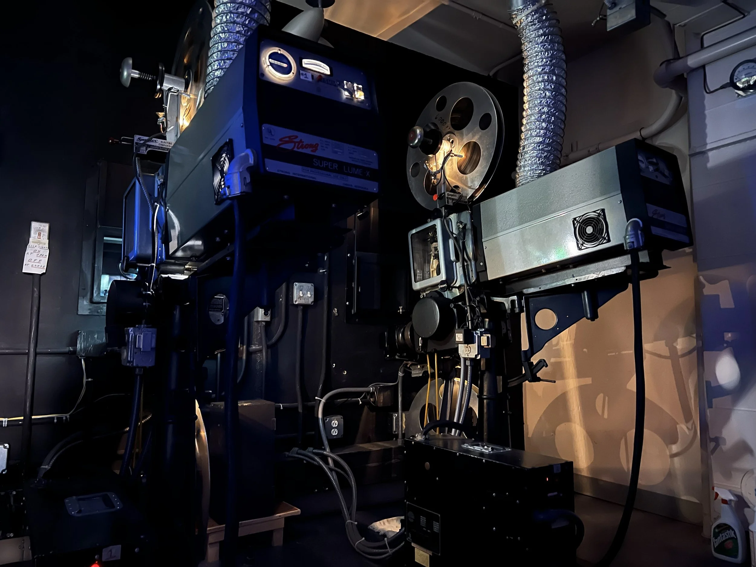 A scientific or industrial laboratory setup with advanced machinery, including a large black device marked 'Strong Super Lumex X', metal pipes, and various electronic components, in a dimly lit environment.