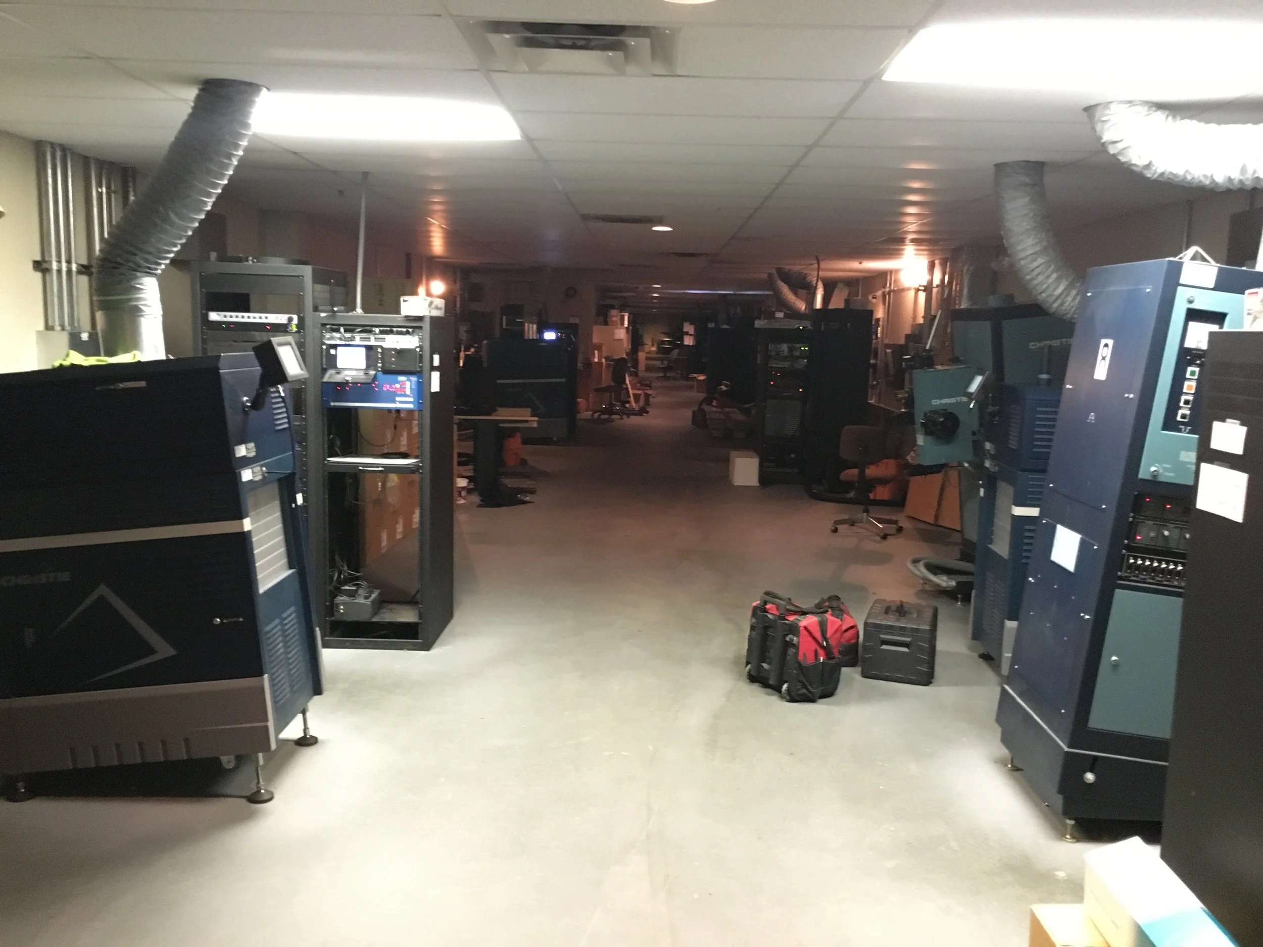 Laboratory or industrial workspace with various electronic equipment, computer monitors, toolboxes, and ventilation ducts on the ceiling.