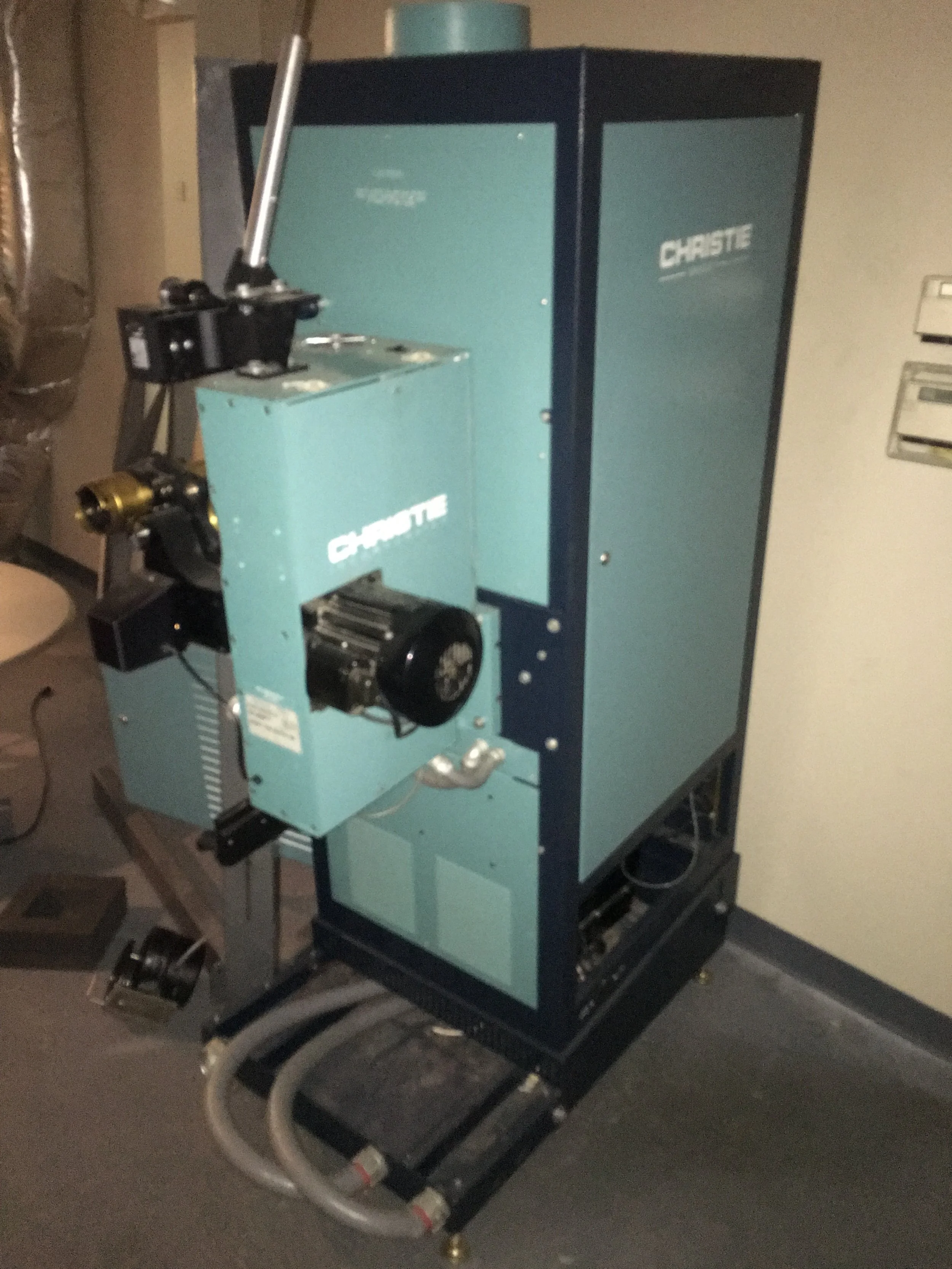 A large blue and black industrial machine with the brand name 'Christe' on it, placed in a room with a beige wall and gray carpet.