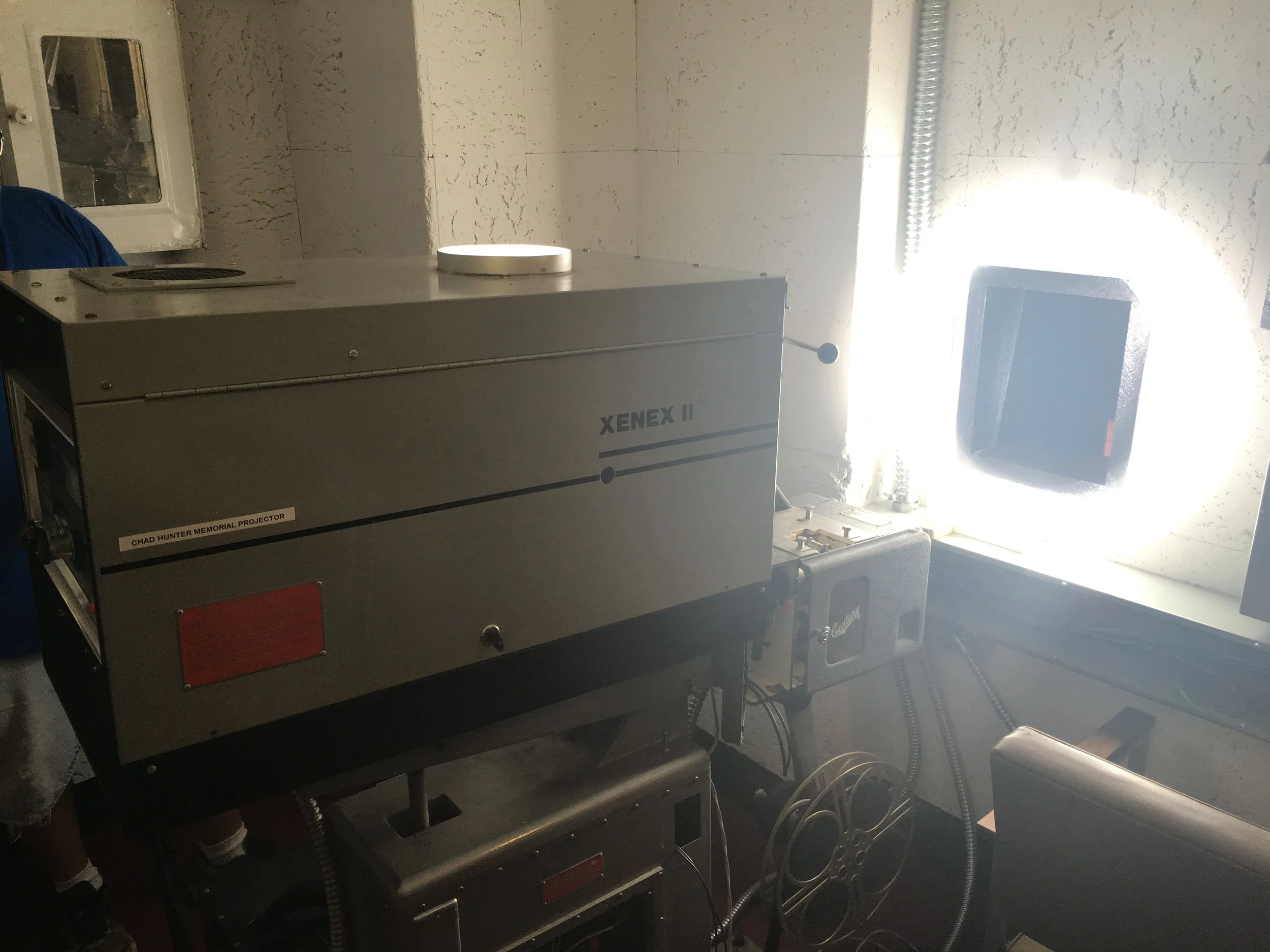 A large scientific instrument labeled 'Xenex II' and 'Chad Hunter Memorial Projector' sits near a window with bright sunlight shining through. Wiring and additional equipment are visible around the device.