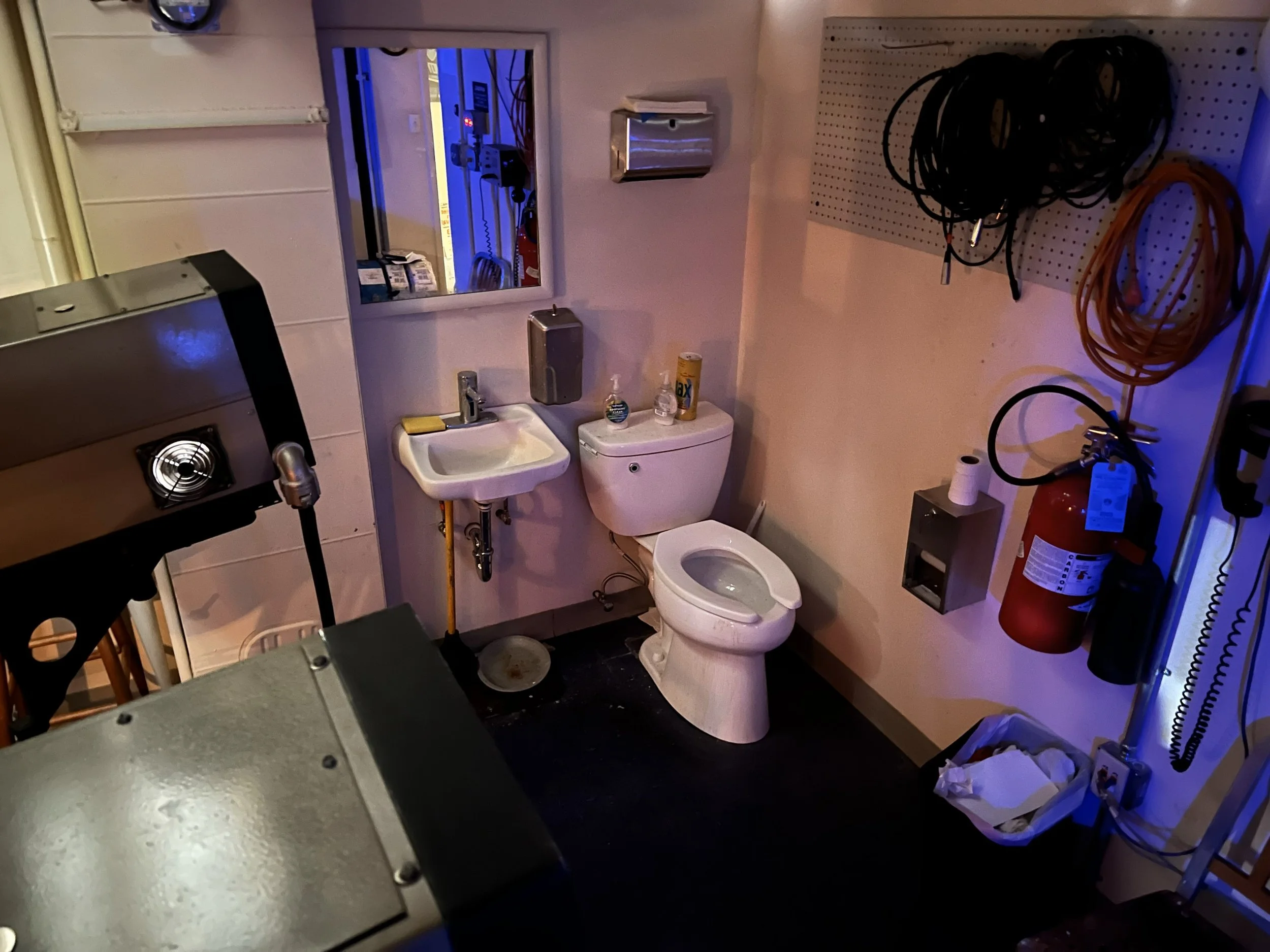 Small bathroom with a toilet, sink, mirror, and Heys sanitizer; contains grooming supplies, cables, fire extinguisher, and a portable heater.