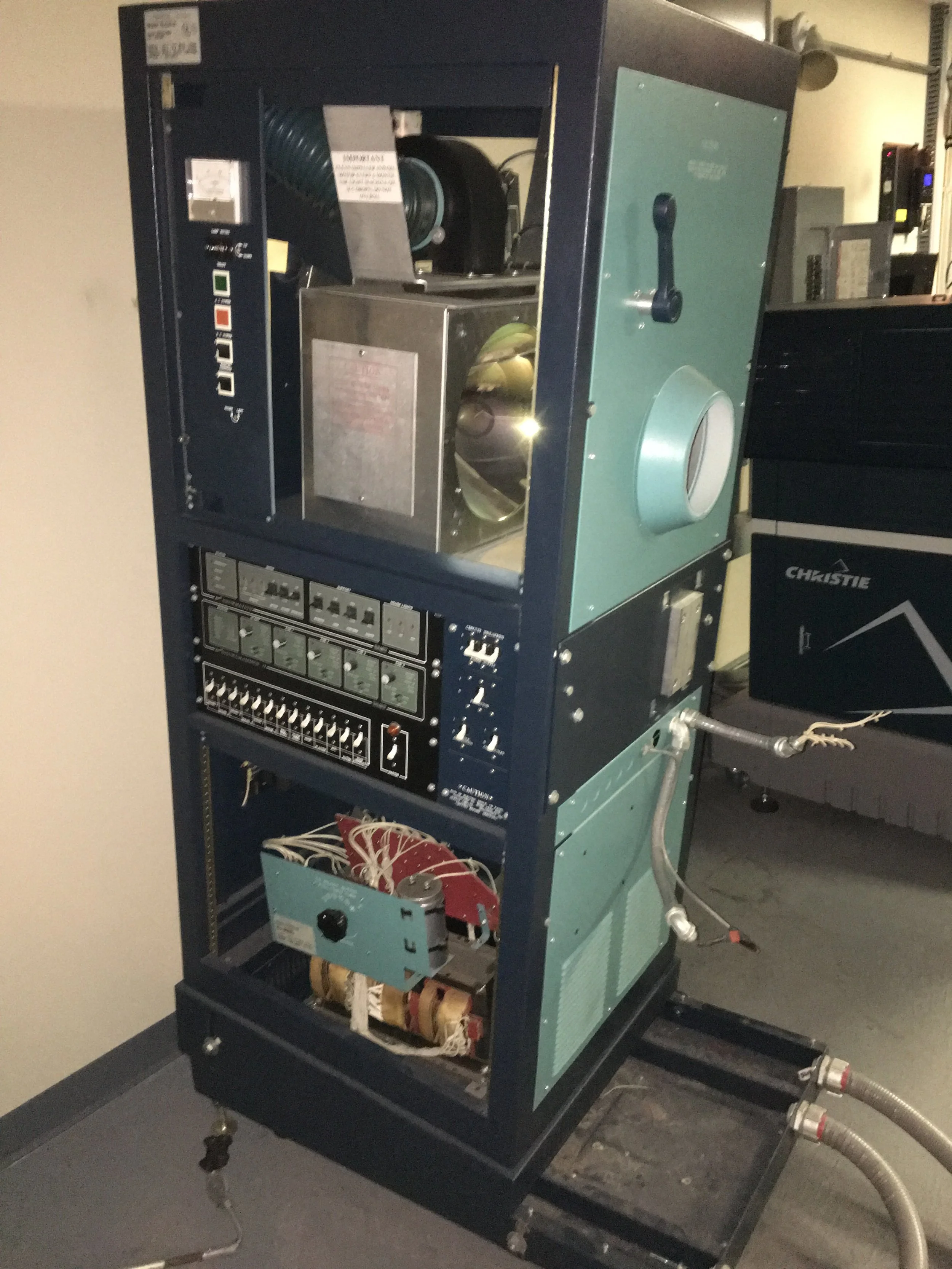 A large industrial HVAC or refrigeration unit with various electrical components and controls, mounted on a black metal frame with wheels in a basement or utility room.