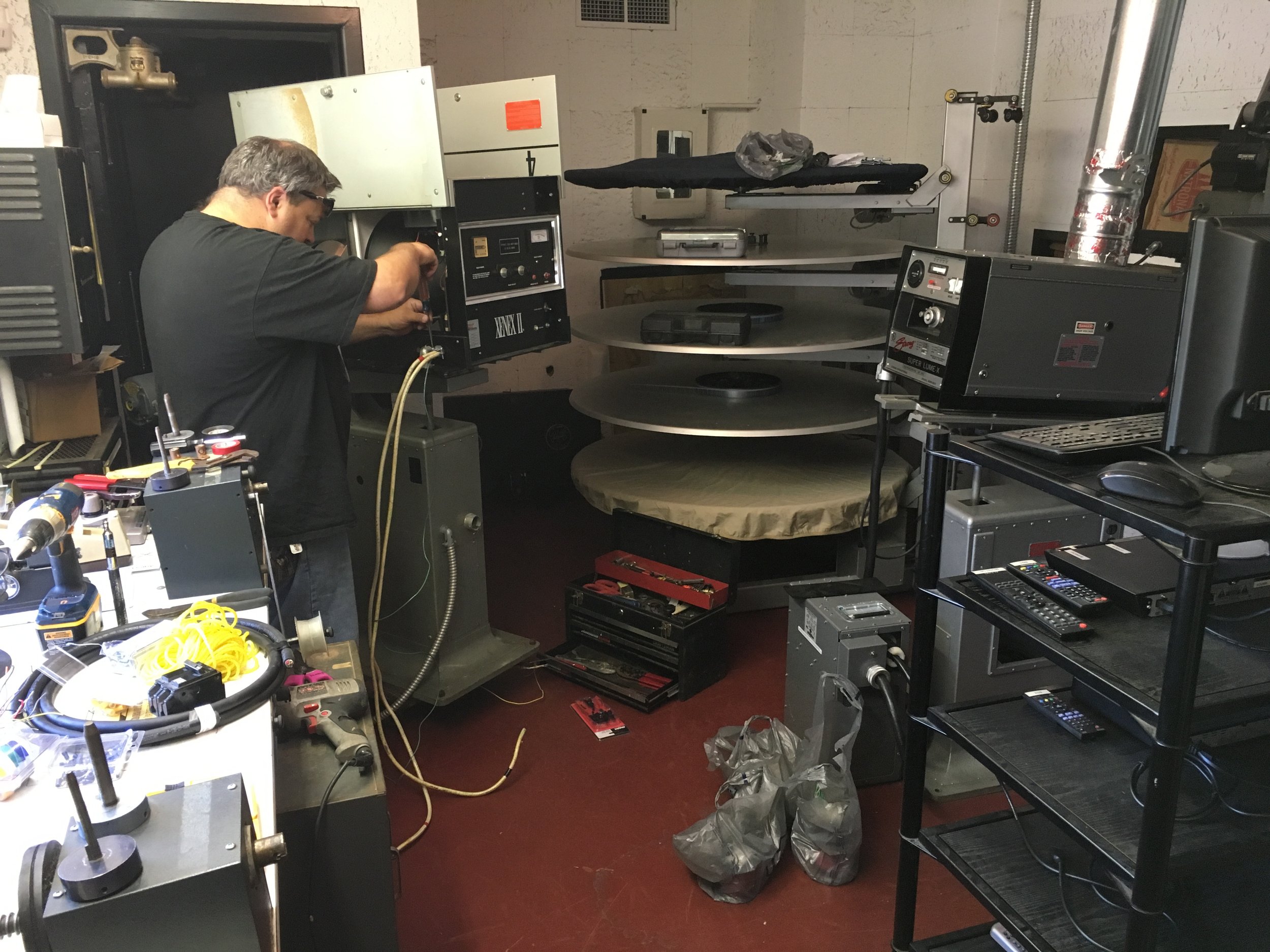 A man working in a lab full of scientific equipment, including machines, tools, cords, and storage shelves.