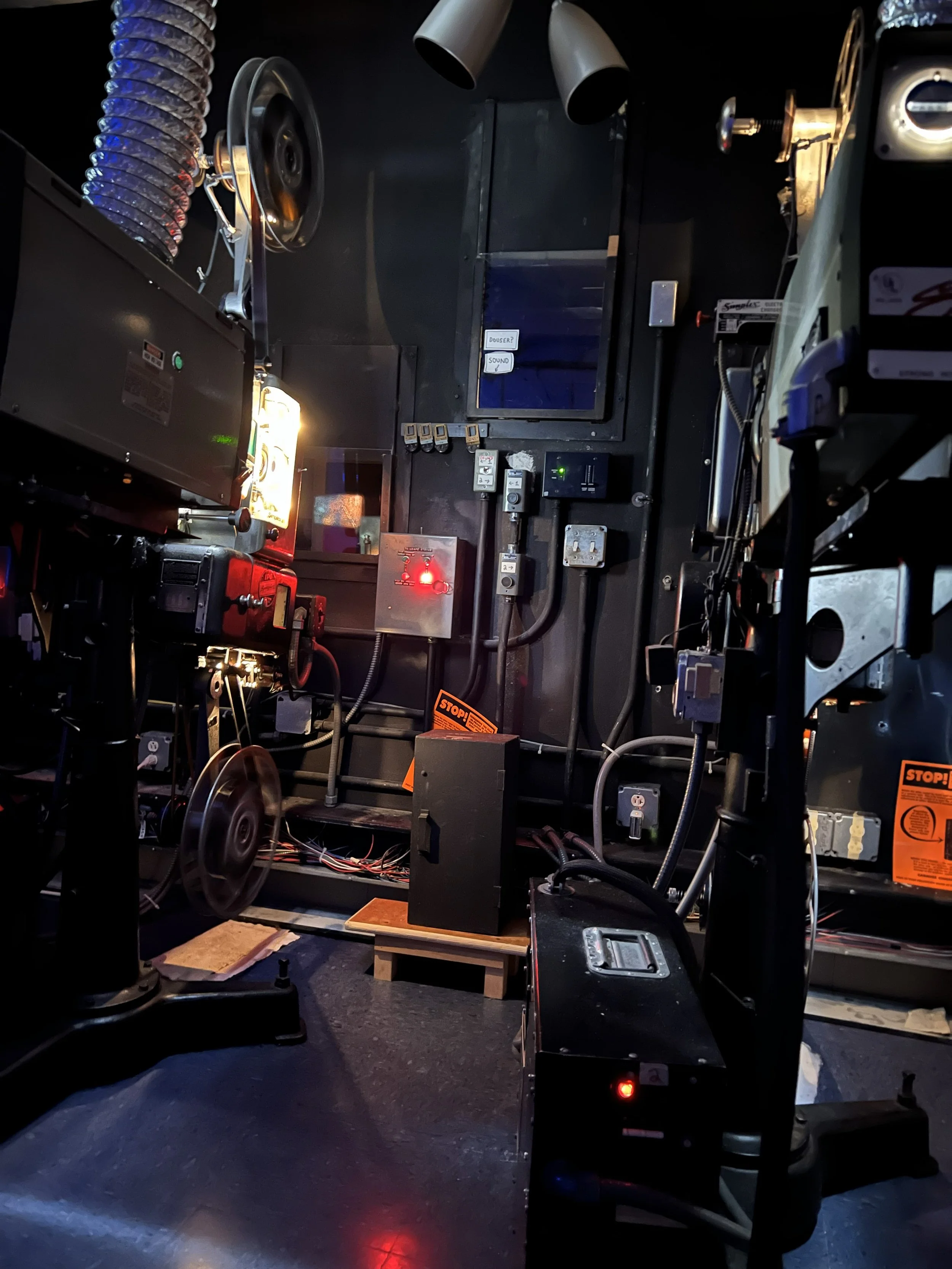 A dark room filled with various electronic equipment, switches, and wires, with a pinkish lamp on the left side.