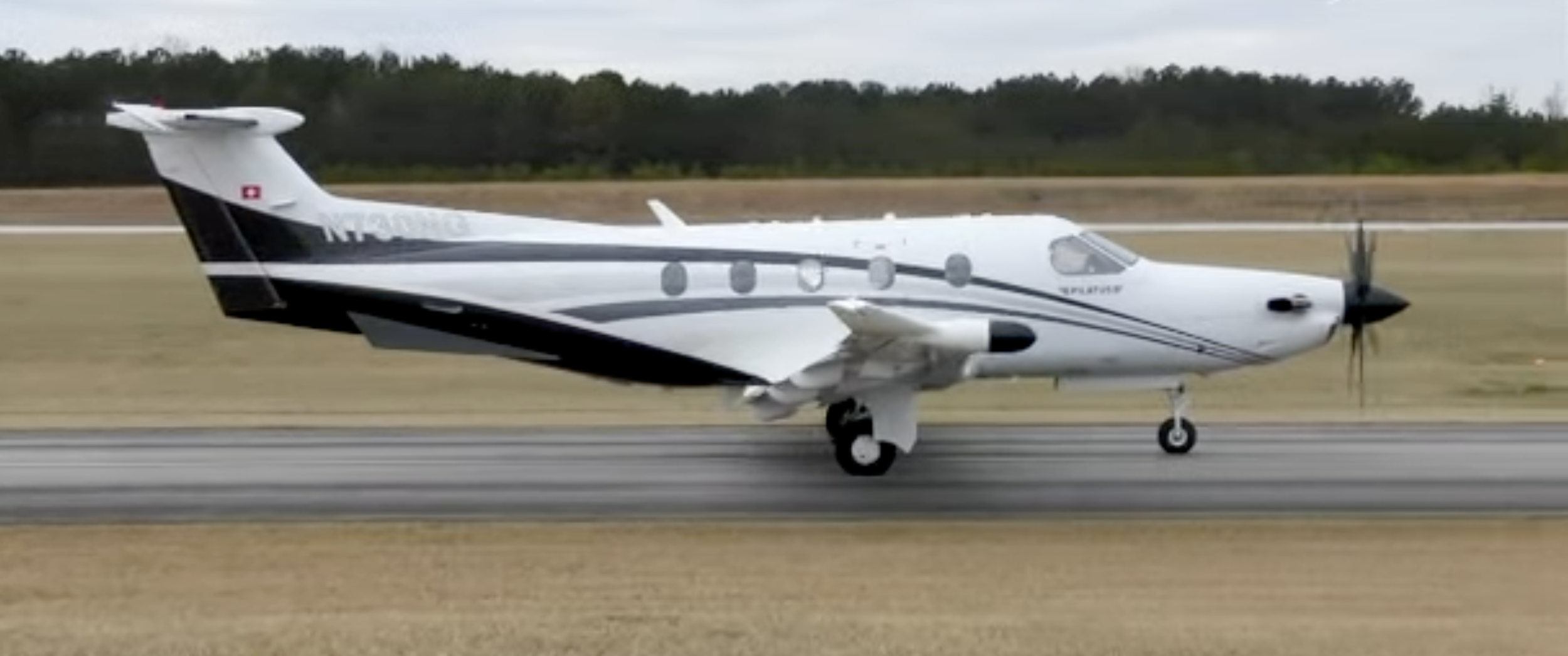 A small propeller airplane on a runway with a grassy field and trees in the background.