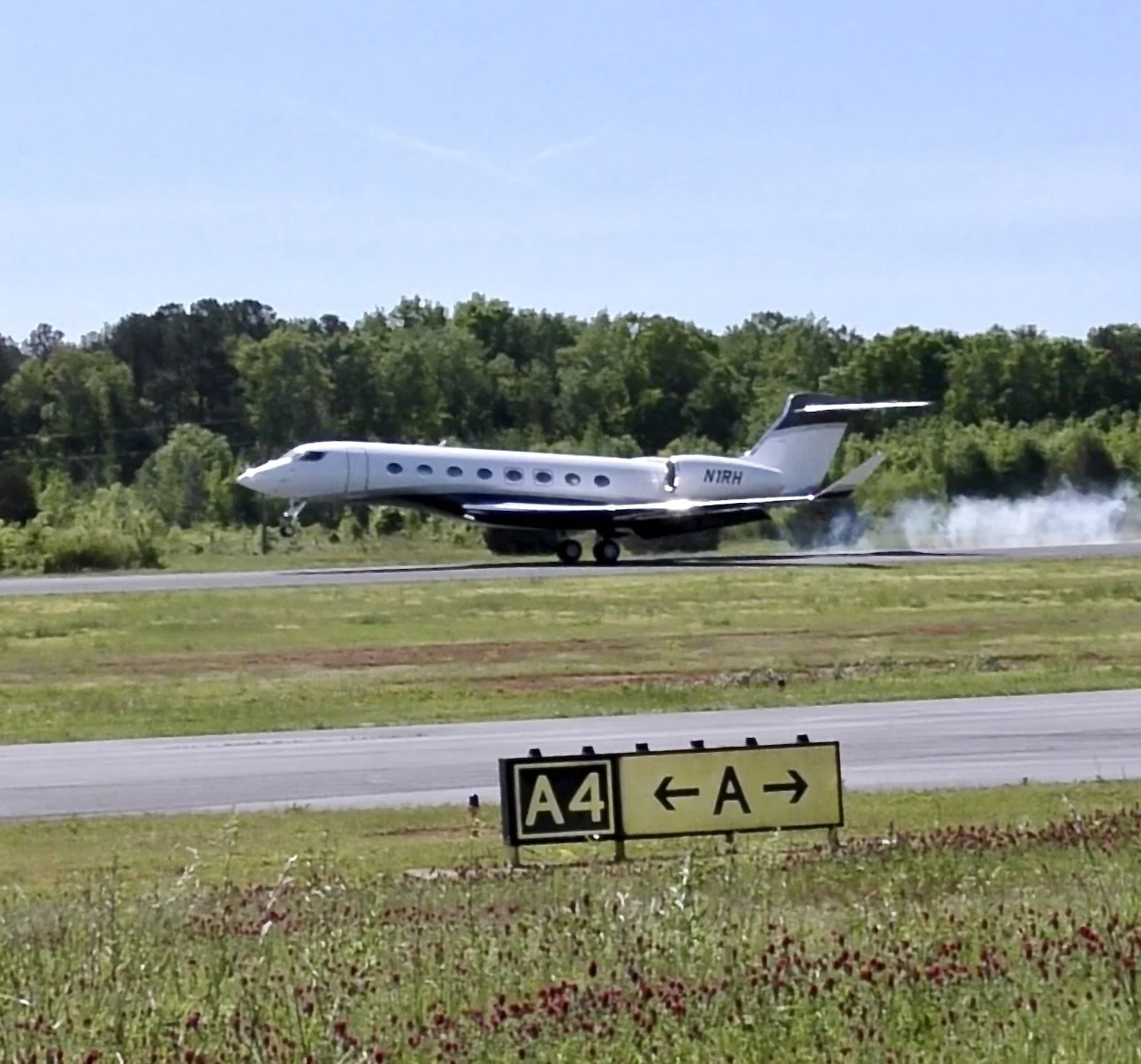 Private jet landing on runway with smoke behind it and a directional sign for taxiways in foreground.