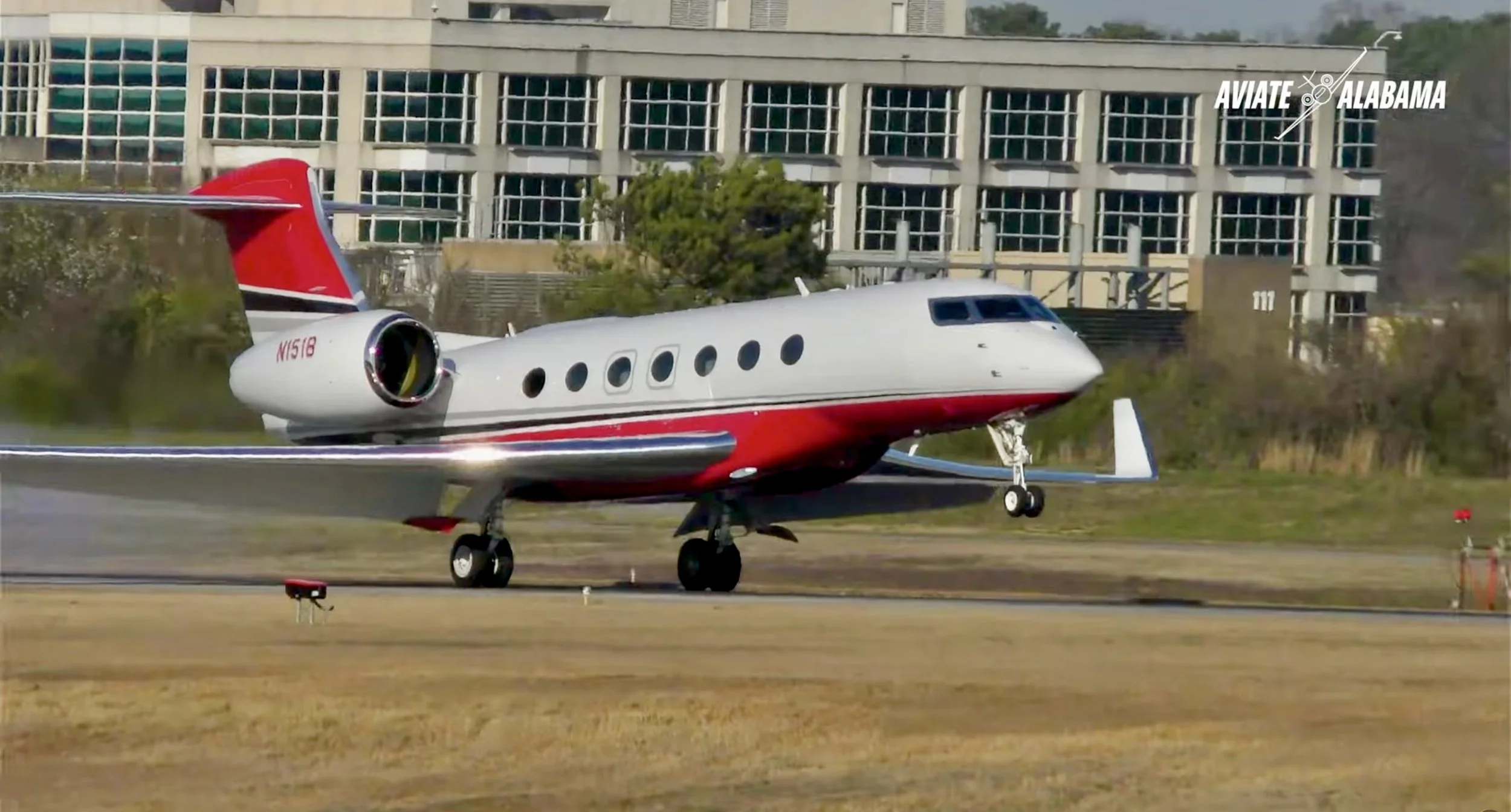 A private jet on a runway with a modern building and trees in the background, with the text 'Aviate Alabama' in the upper right corner.