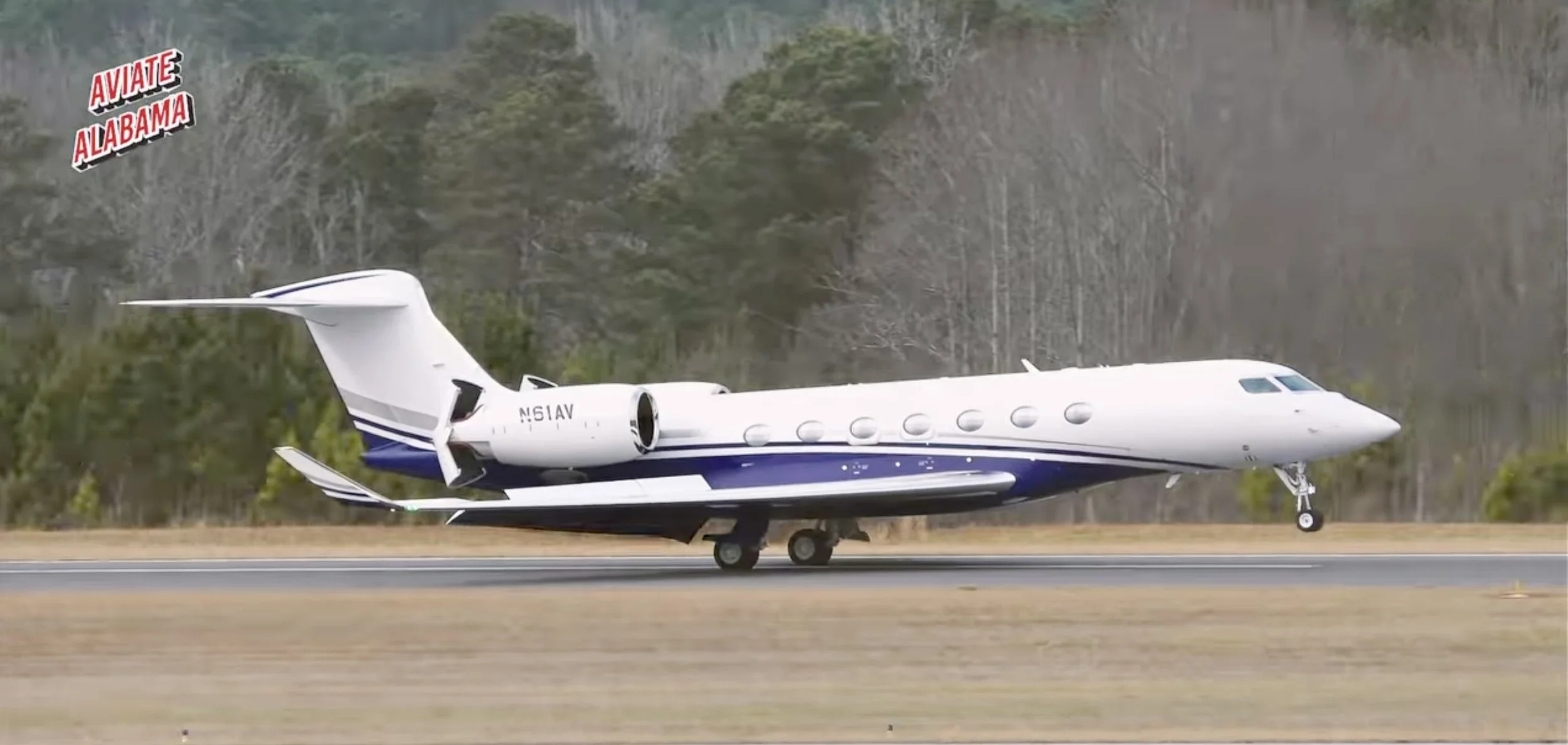 A private jet airplane on a runway with a wooden and tree-lined background.