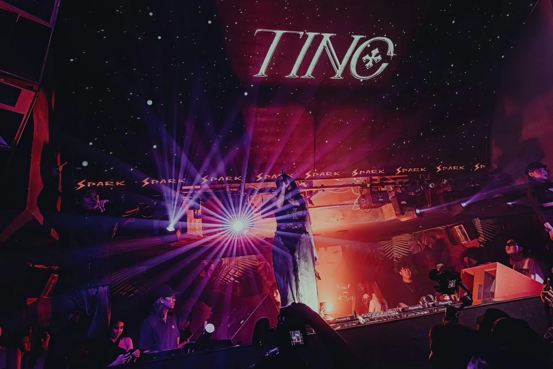 A nightclub scene with dancers on stage, colorful laser lights, and a DJ booth, with a sign reading 'TINO' above.