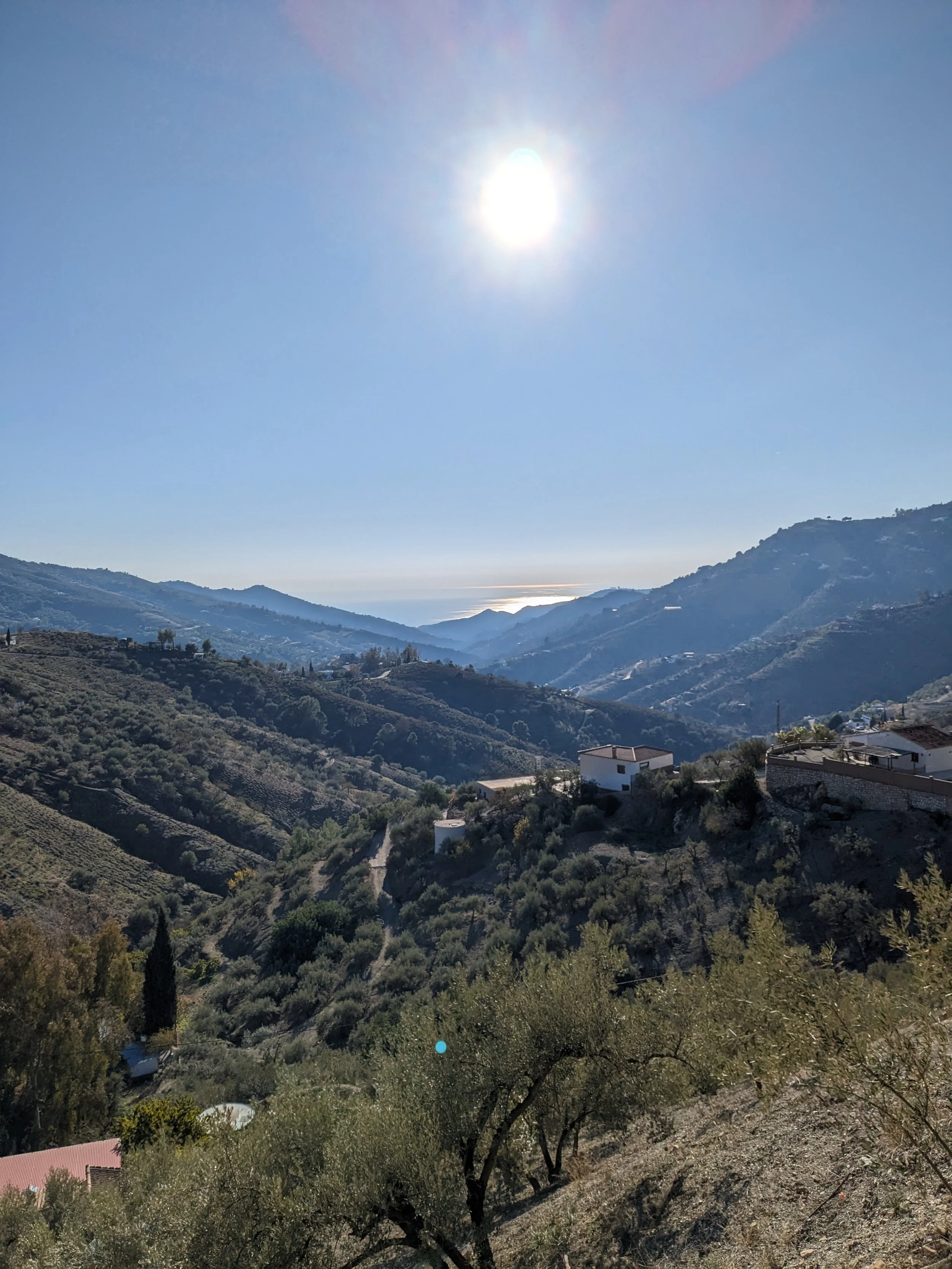 Sun shining over a mountain valley with houses and trees.