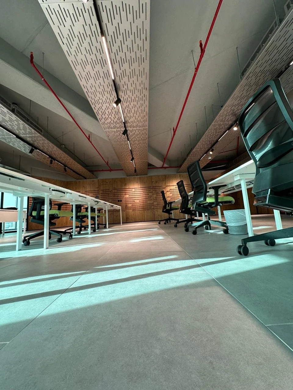 Empty modern office conference room with chairs and tables, wood panel wall, ceiling with acoustic panels and industrial red pipes.
